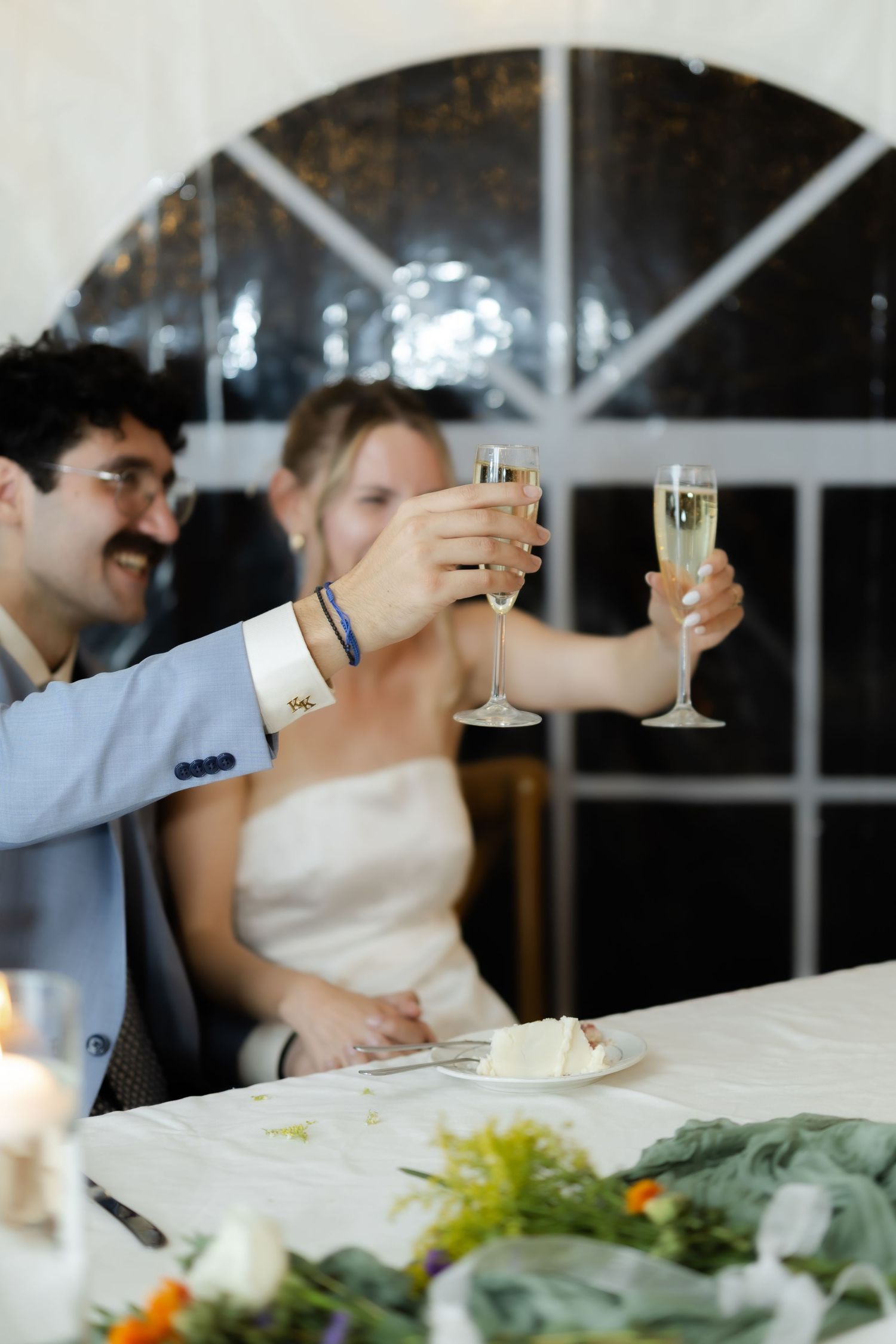 Bride and groom raising champagne flutes in a toast at their wedding reception dinner table.