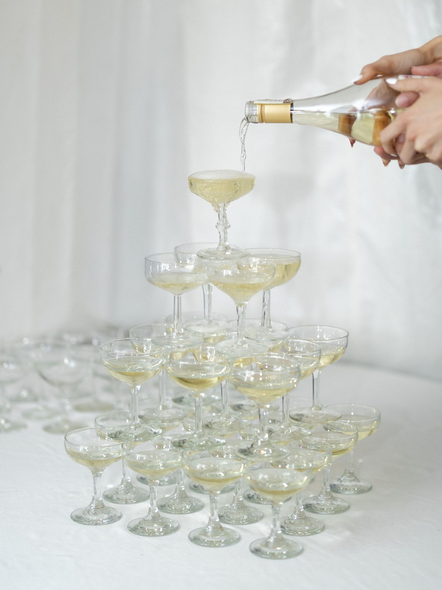 Champagne tower with coupe glasses being filled from a bottle at an elegant celebration event.