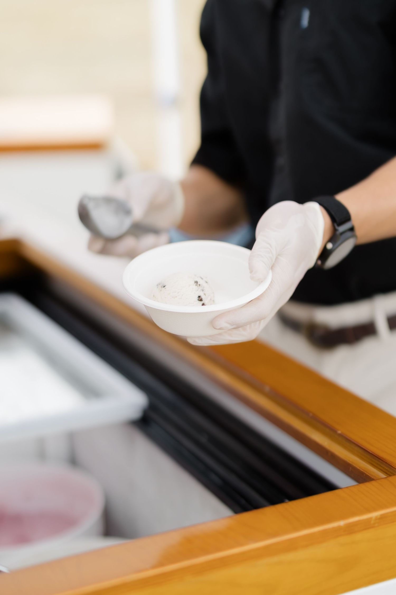 Chef in black uniform and white gloves holding a white bowl at a food service counter.