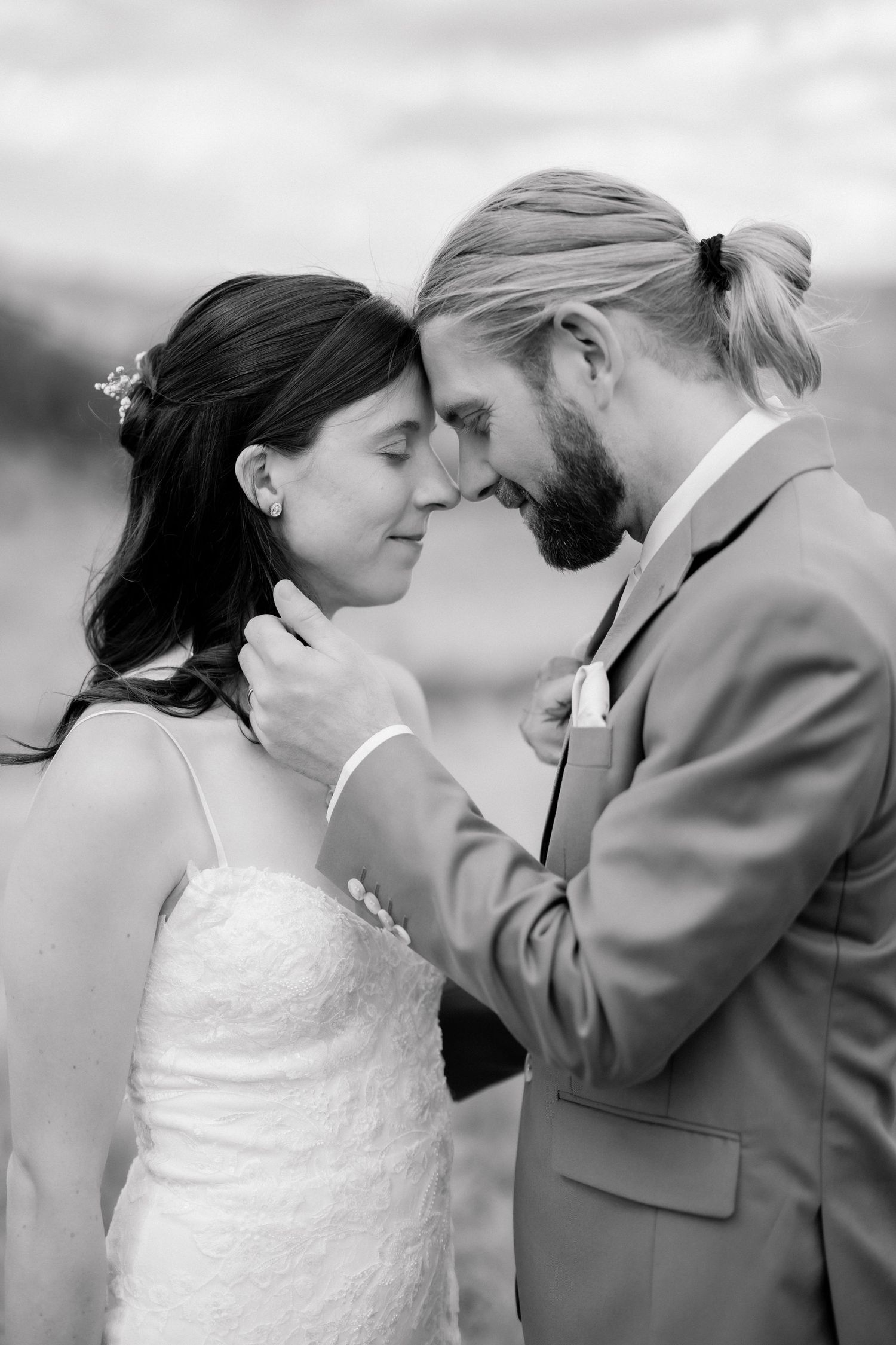 Black and white wedding photo of bride and groom touching foreheads tenderly, groom in suit holding bride's face.