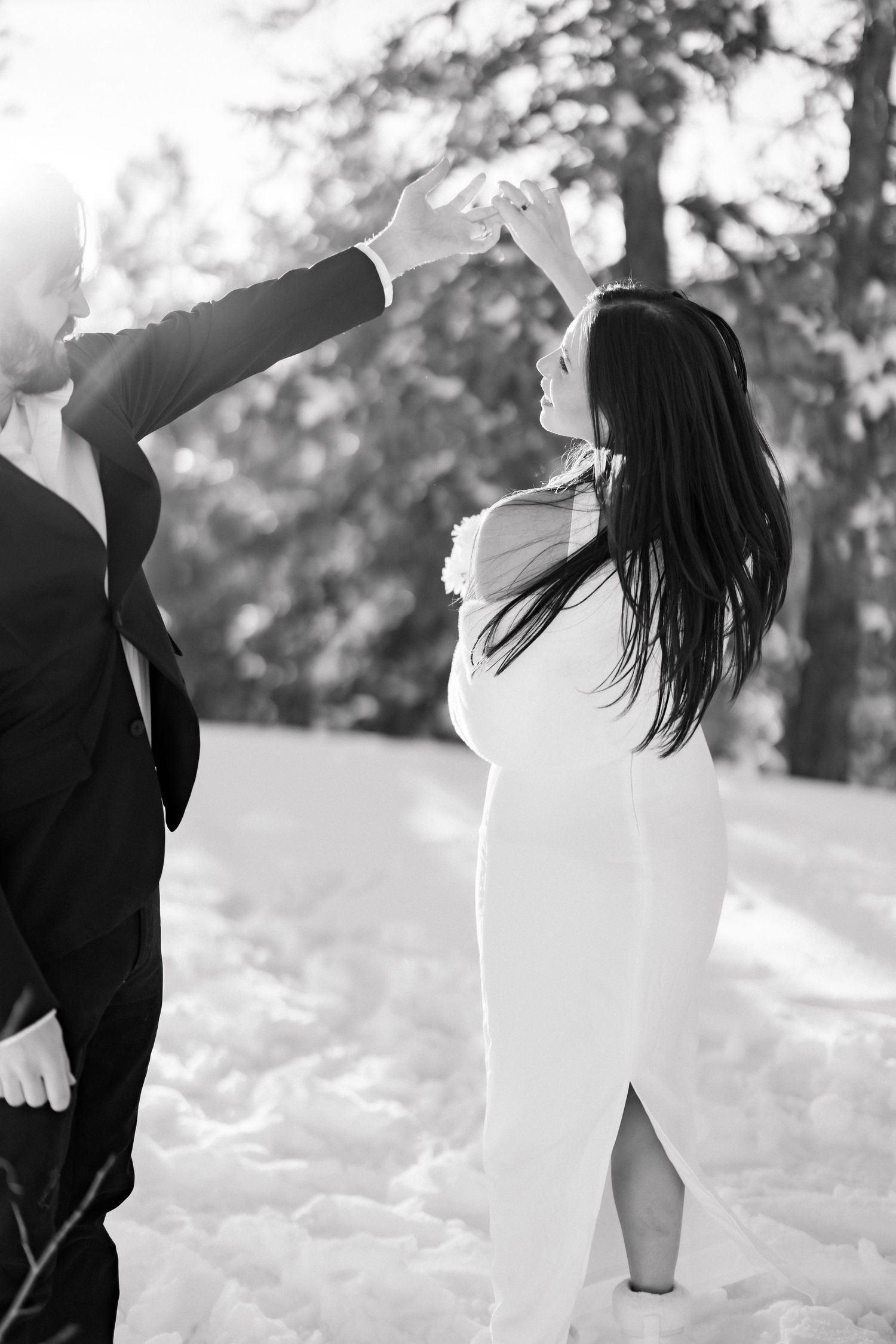 Bride and groom dance together in snowy winter landscape, elegant black and white wedding photo.