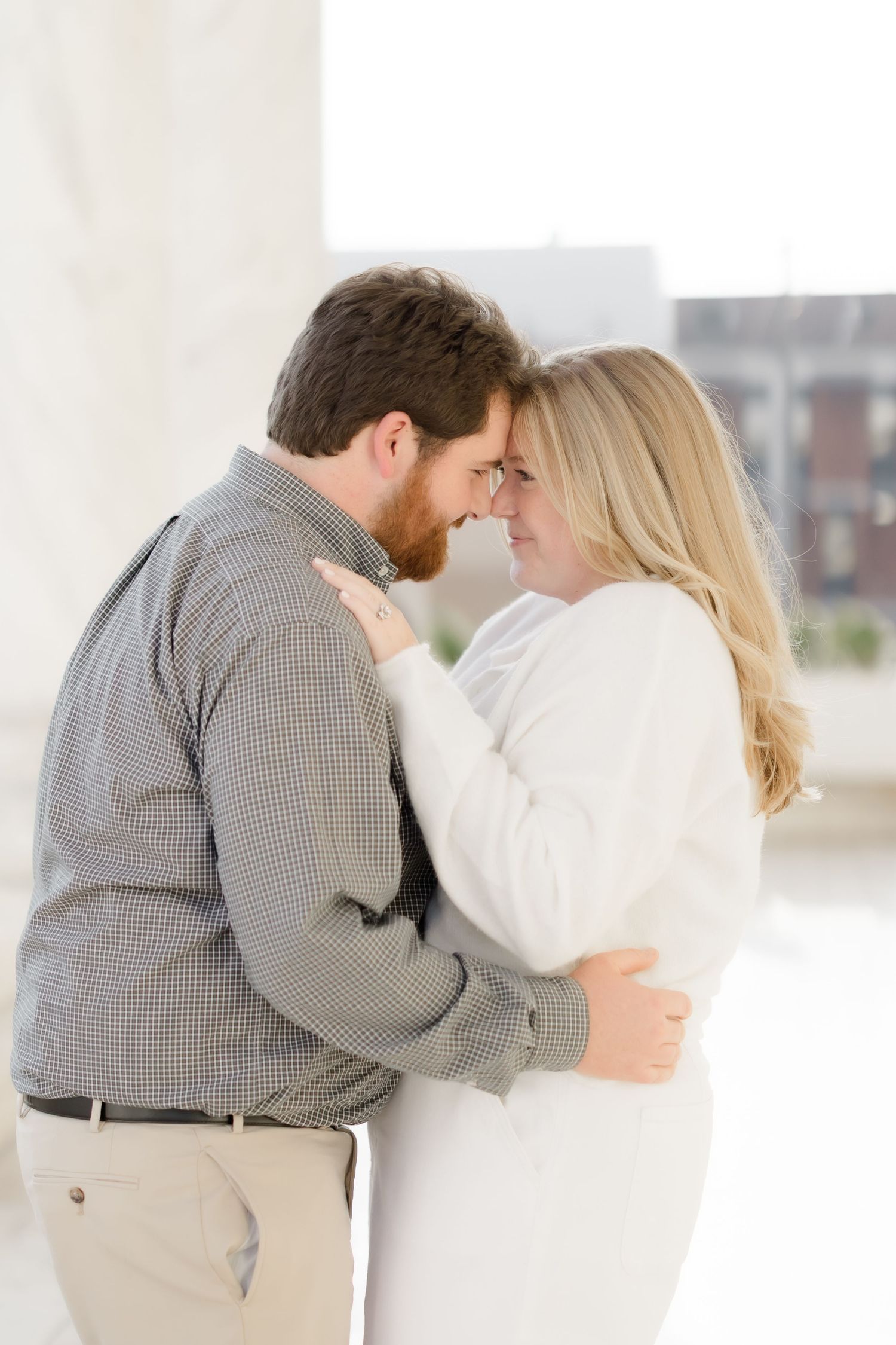 Black and white photo of a couple embracing with foreheads touching near marble columns.