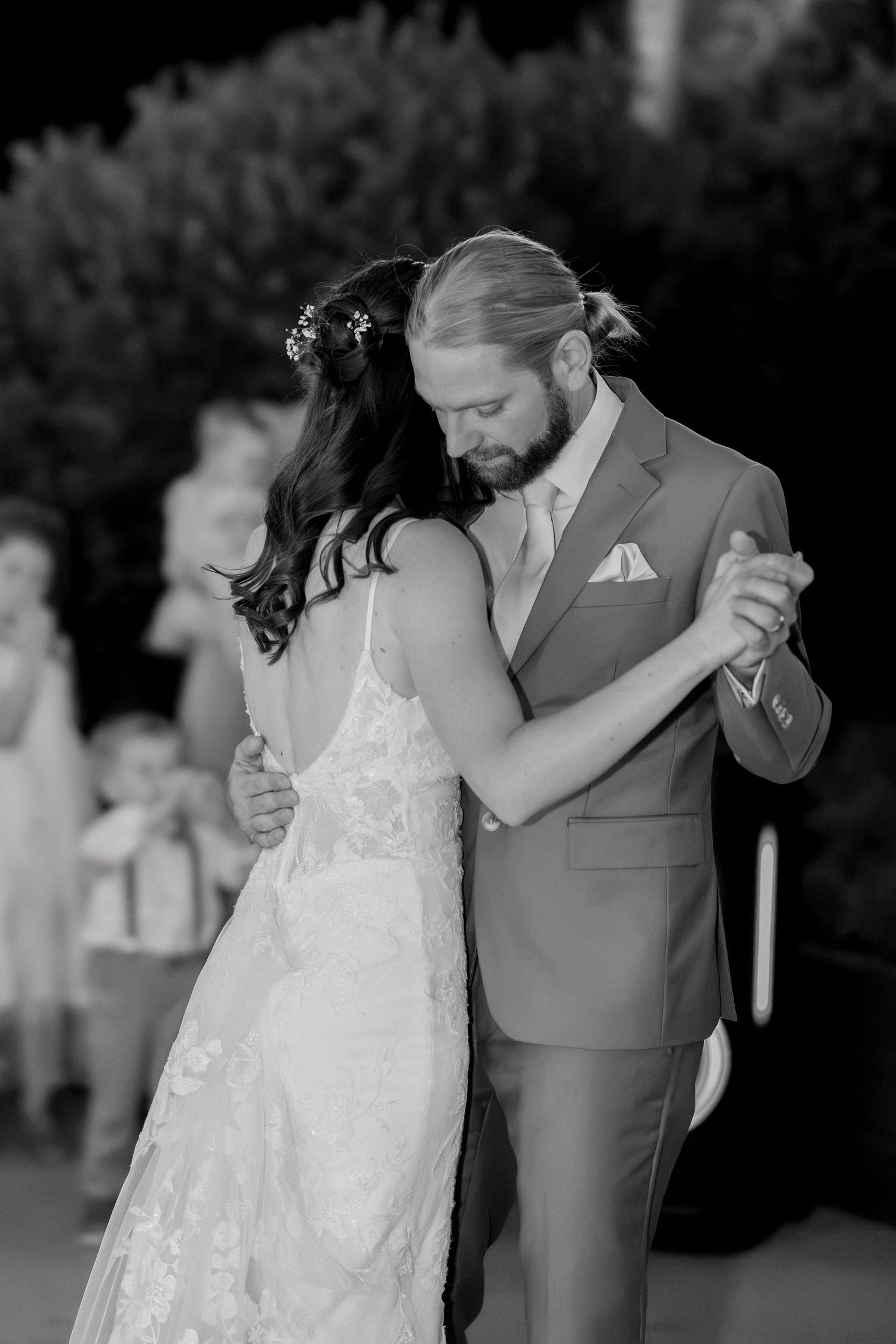 Bride and groom share romantic first dance outdoors, bride in lace wedding dress with floral hair accessories.