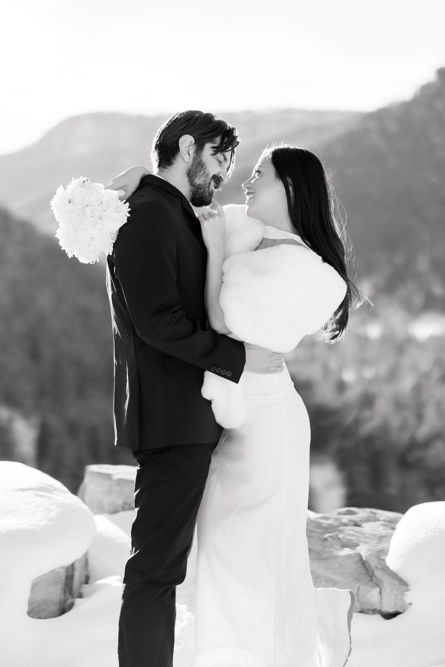 Black and white photo of bride and groom laughing together in snowy mountain wedding setting.