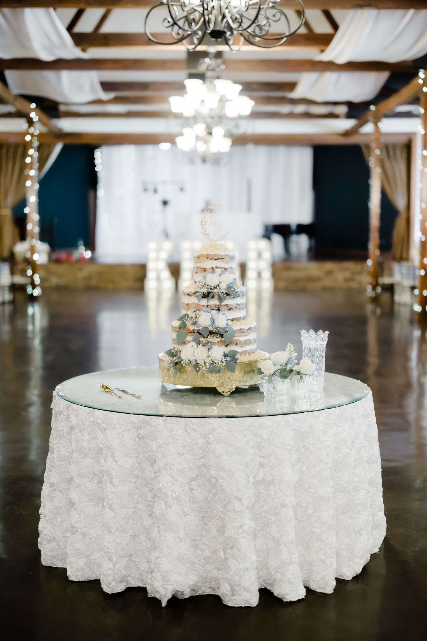 Elegant wedding cake on a round table with white lace tablecloth in a decorated reception hall.