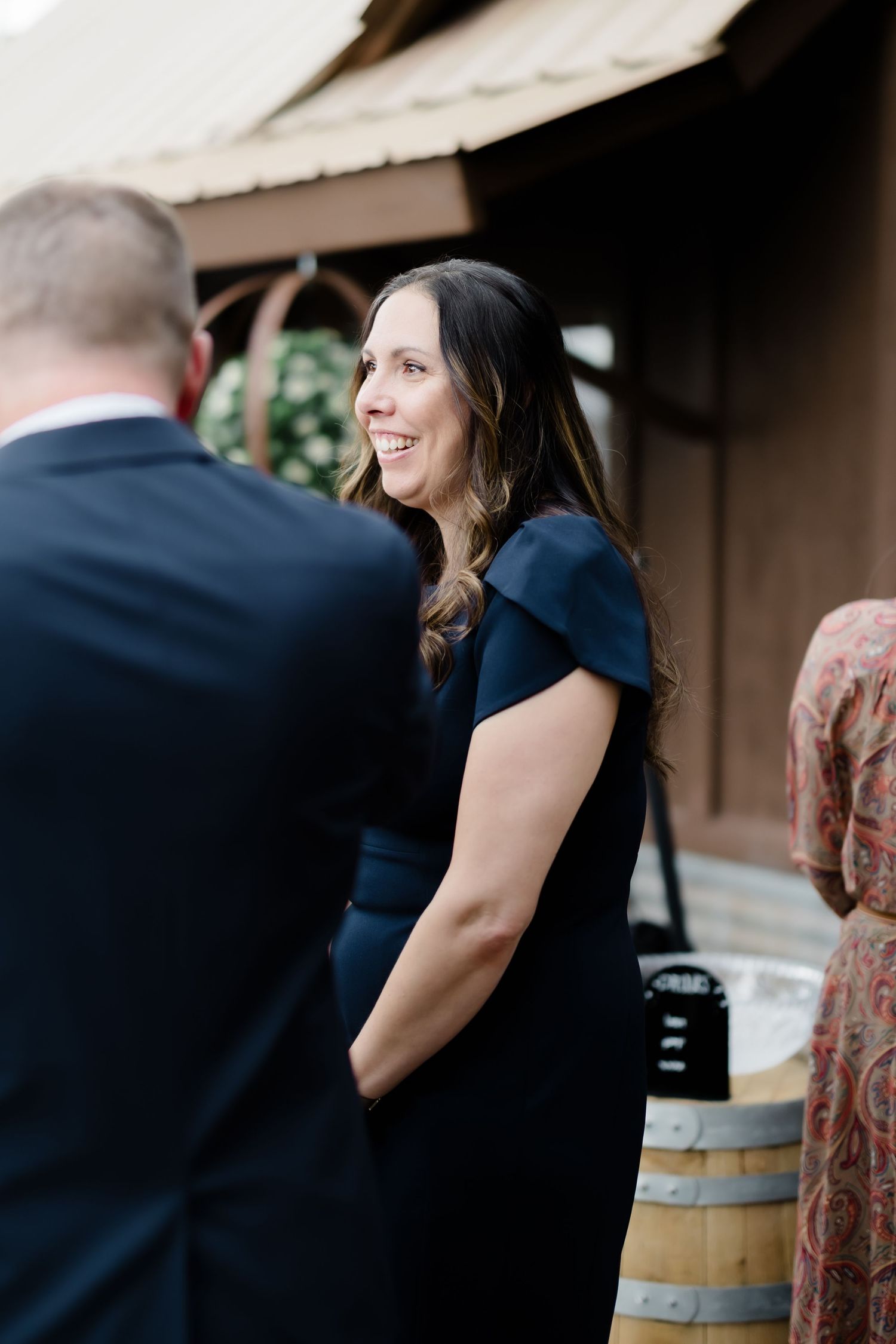 Smiling woman in navy dress at outdoor wedding venue with wooden barrel decoration.