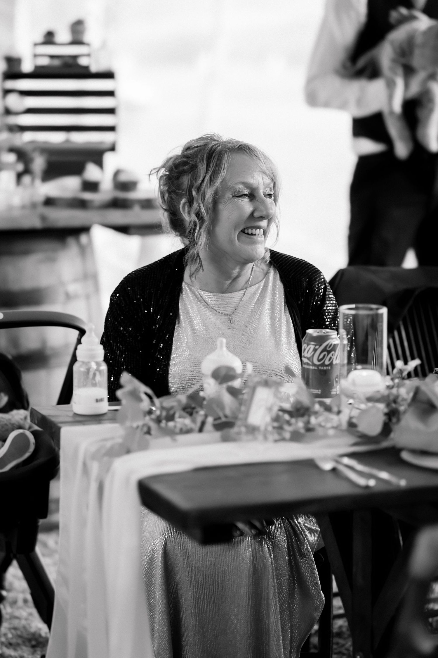 Black and white photo of smiling wedding guest seated at decorated reception table with Coca-Cola.