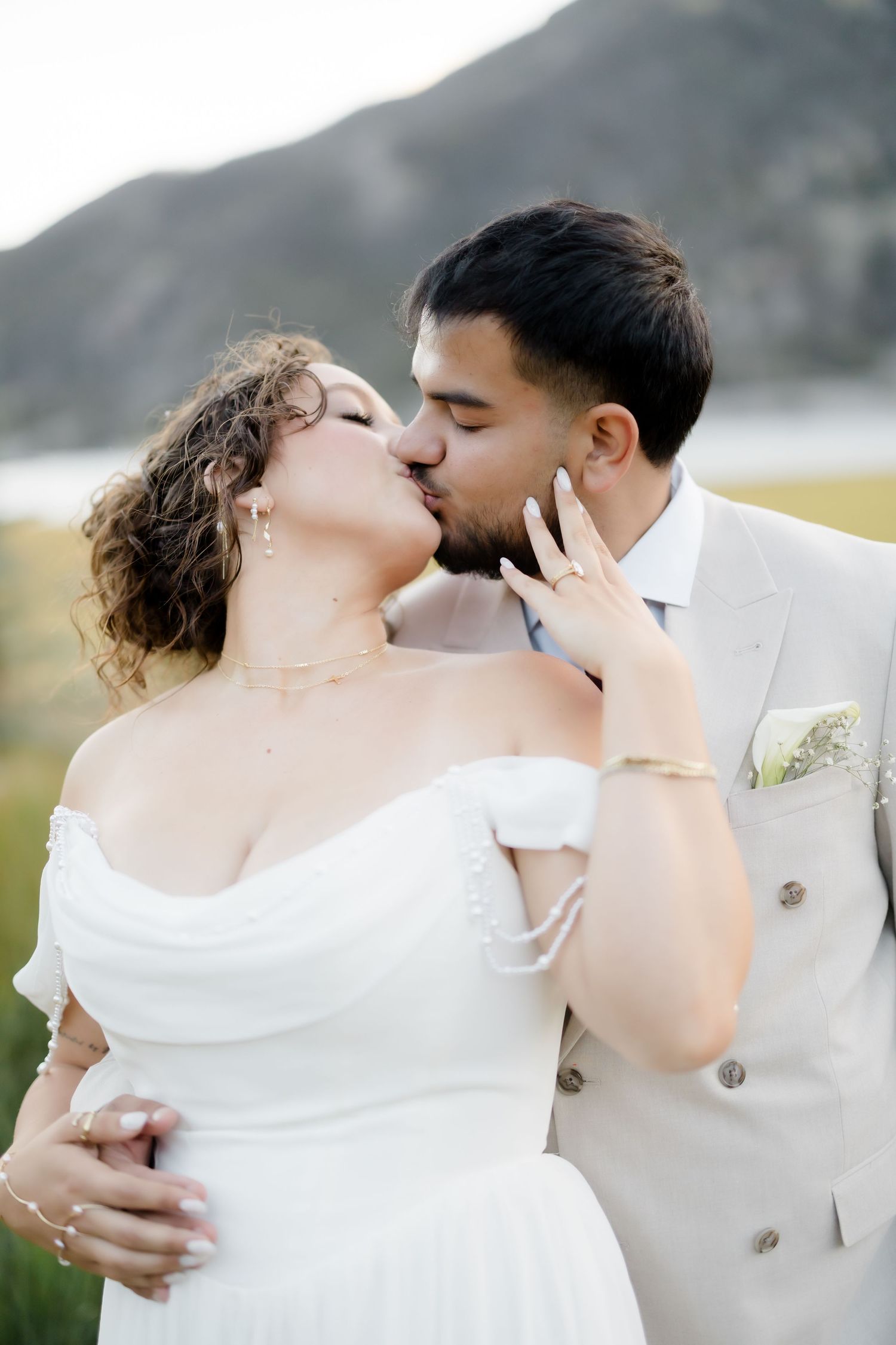 Bride and groom sharing a romantic kiss outdoors with mountain backdrop on their wedding day.