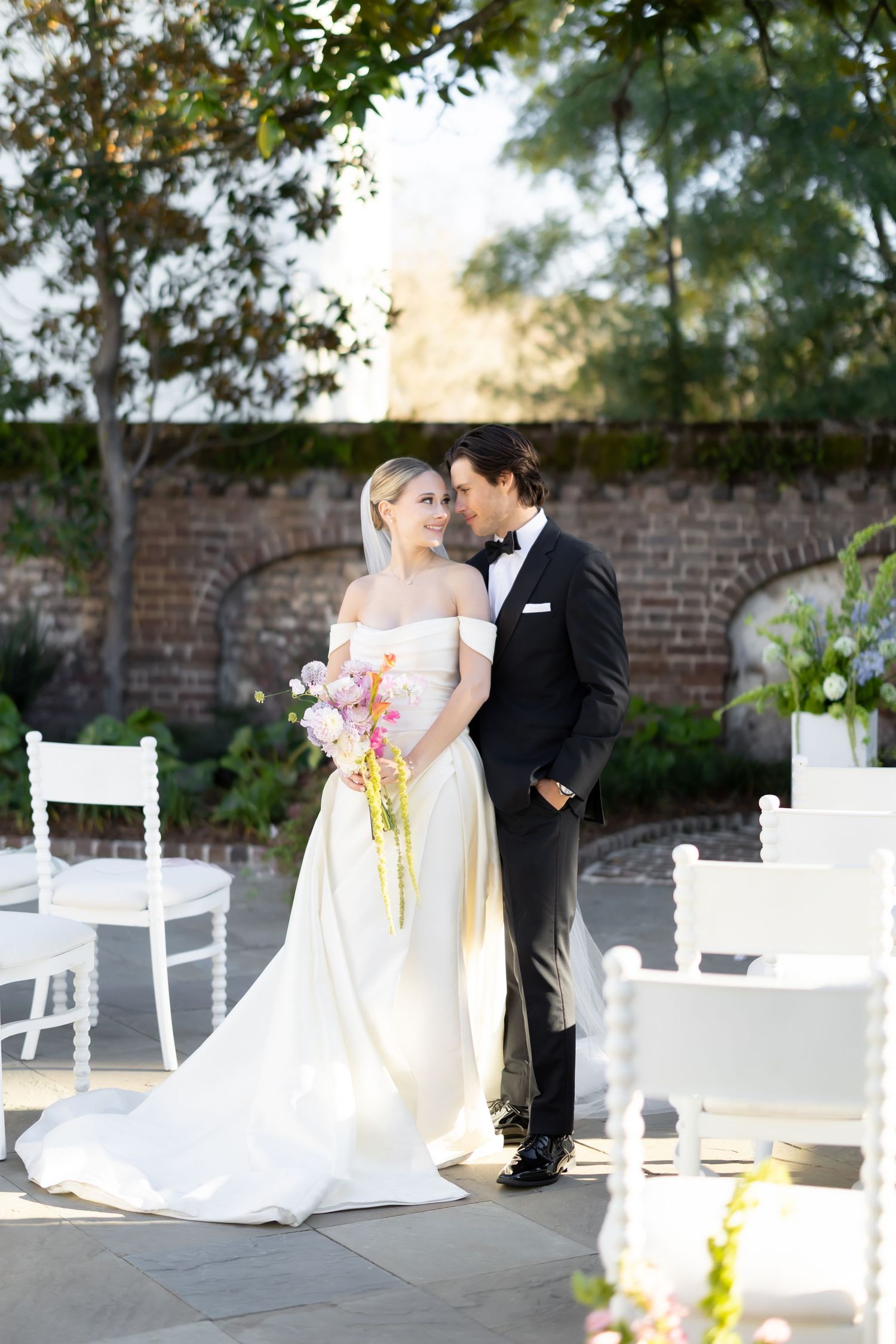 A romantic wedding scene with white chairs and a brick wall backdrop.