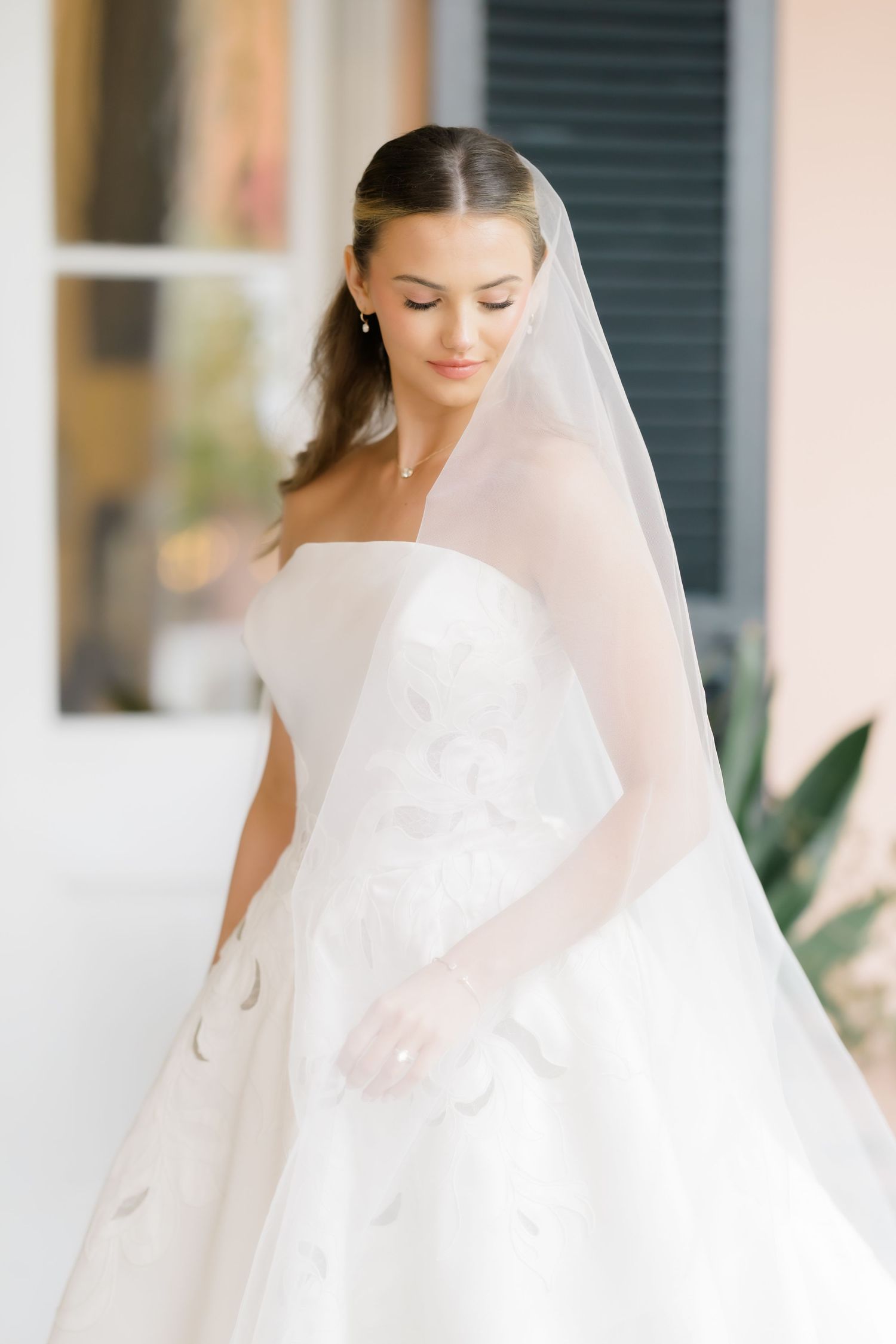Elegant bride in white wedding dress and veil standing on porch.