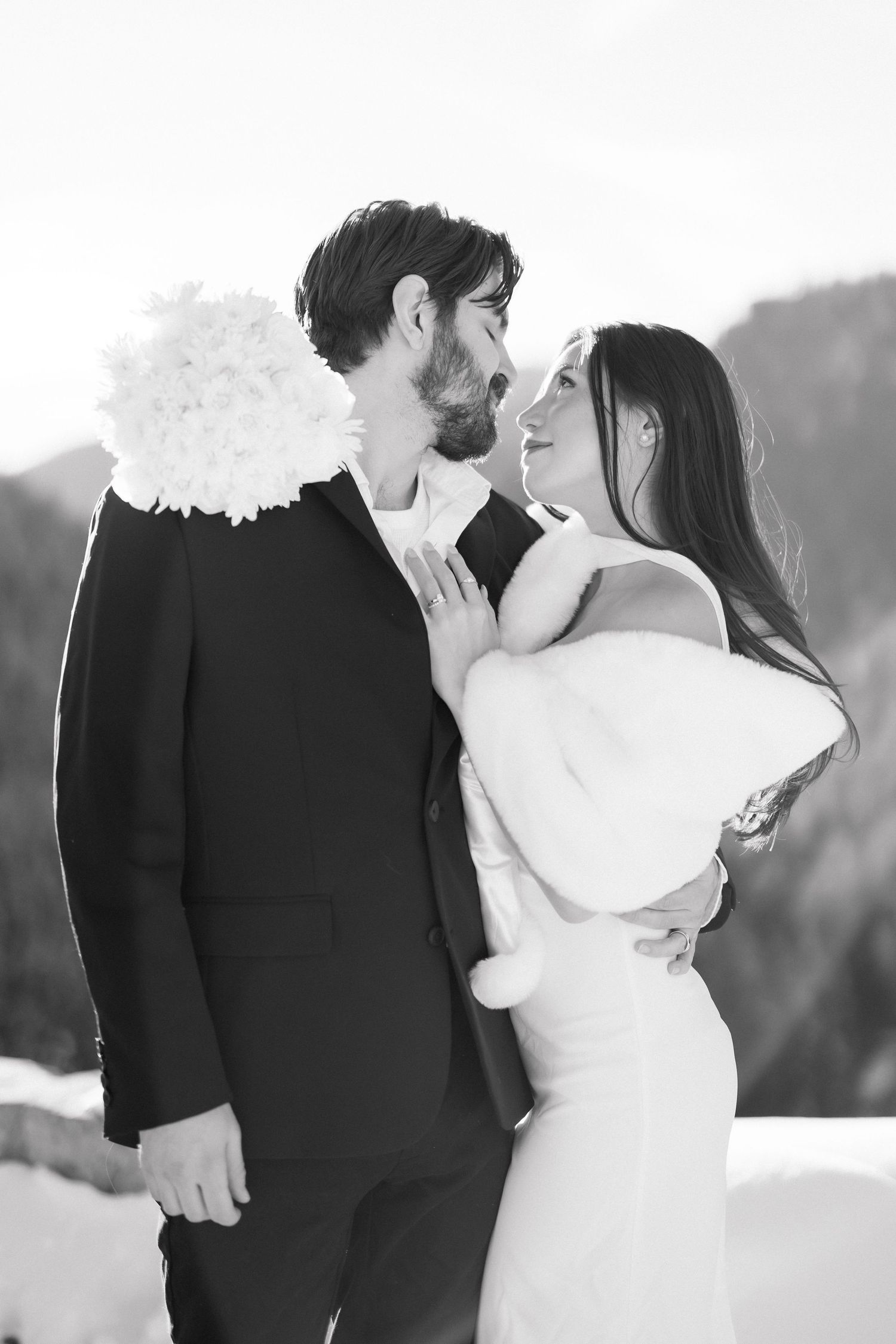 Black and white portrait of smiling bride and groom face to face in snowy mountain setting.