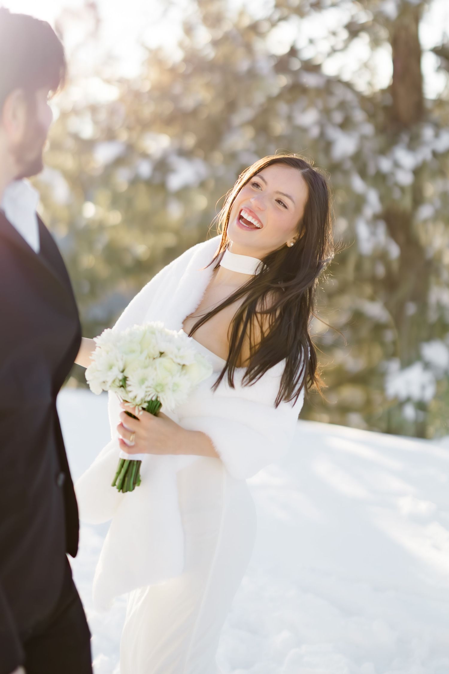 Joyful bride in white gown laughing with groom during winter wedding photo session outdoors.
