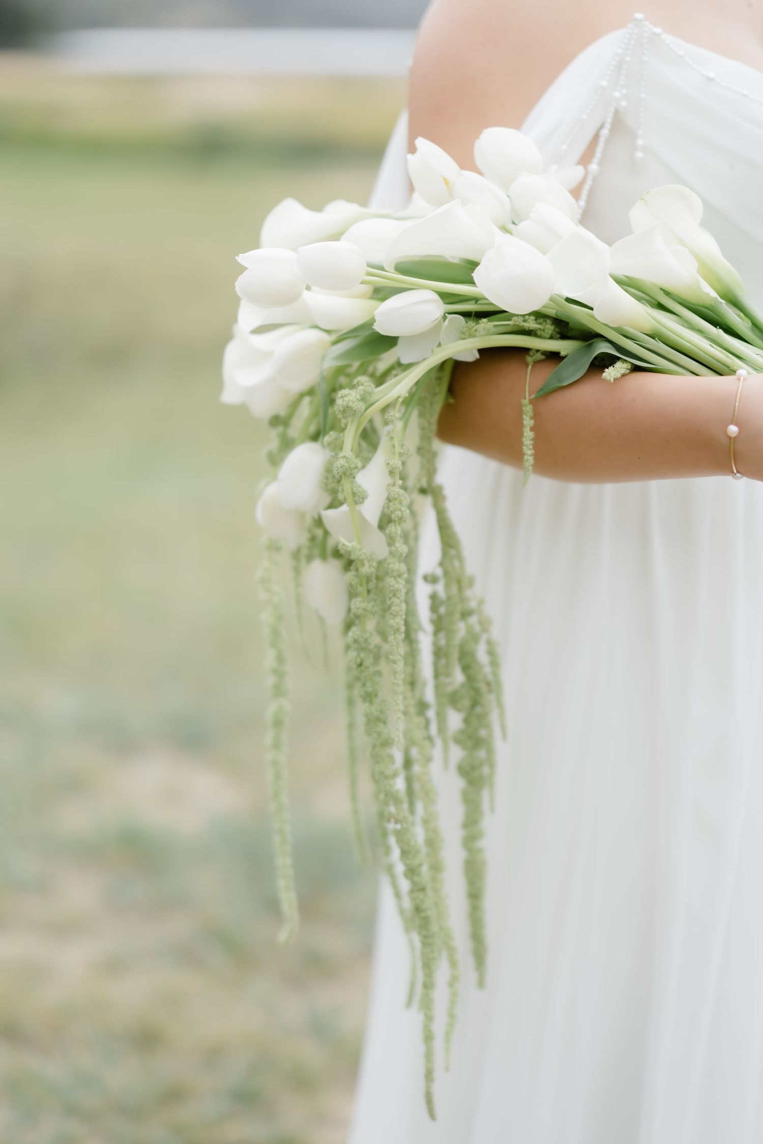 Bride holding white tulip wedding bouquet with cascading green amaranthus in an outdoor setting.