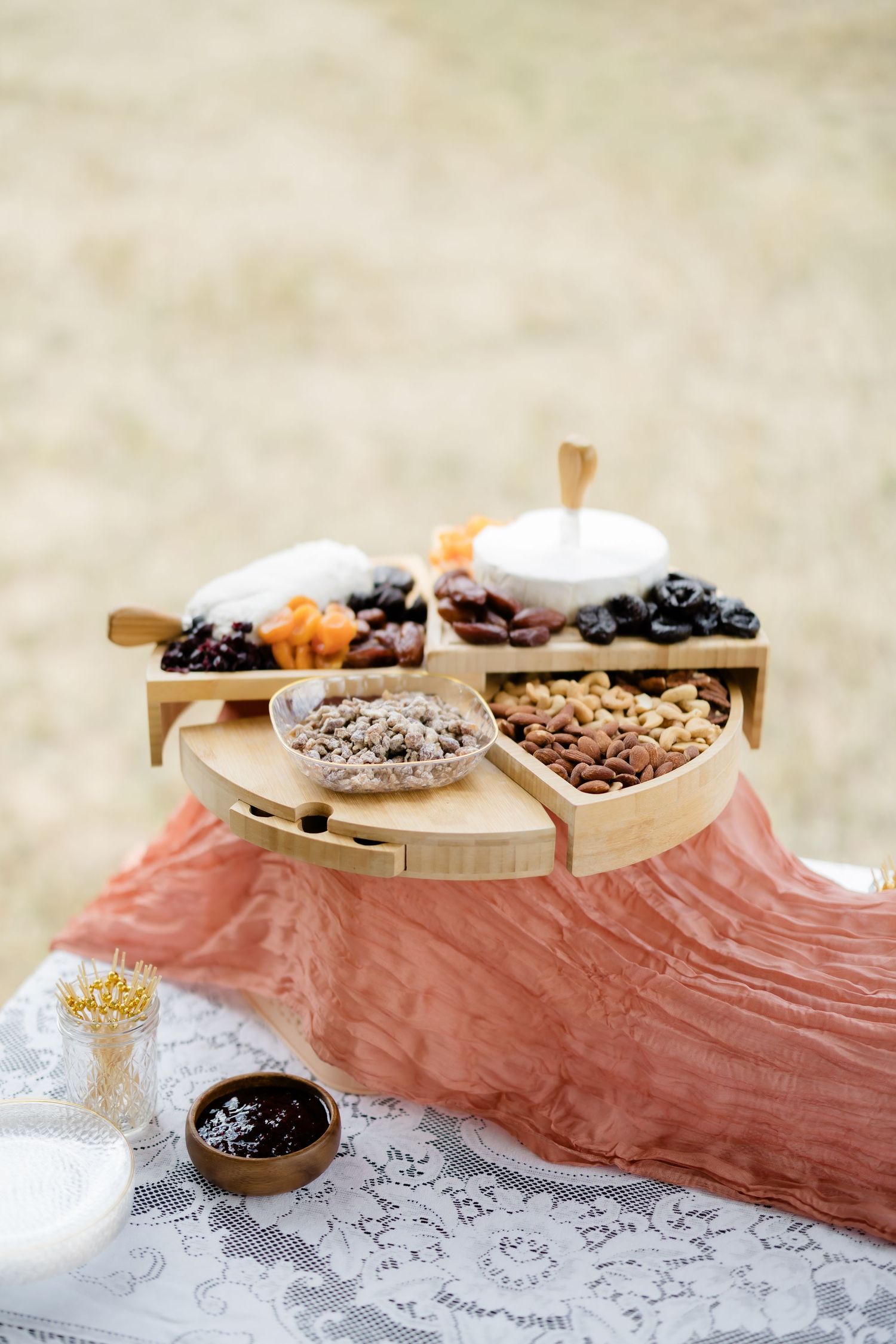 Elegant outdoor wedding charcuterie board with nuts, dried fruits, and cheese displayed on a wooden tiered serving stand.