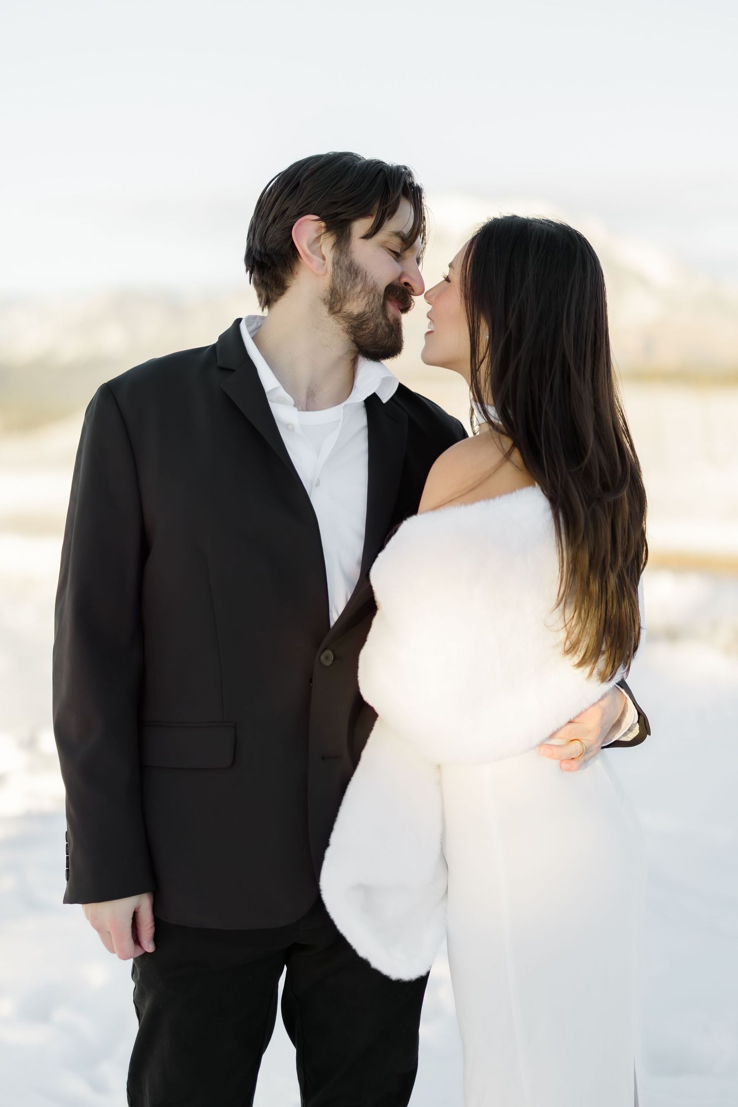 Bride and groom sharing a tender almost-kiss moment in a bright snowy winter wedding landscape.