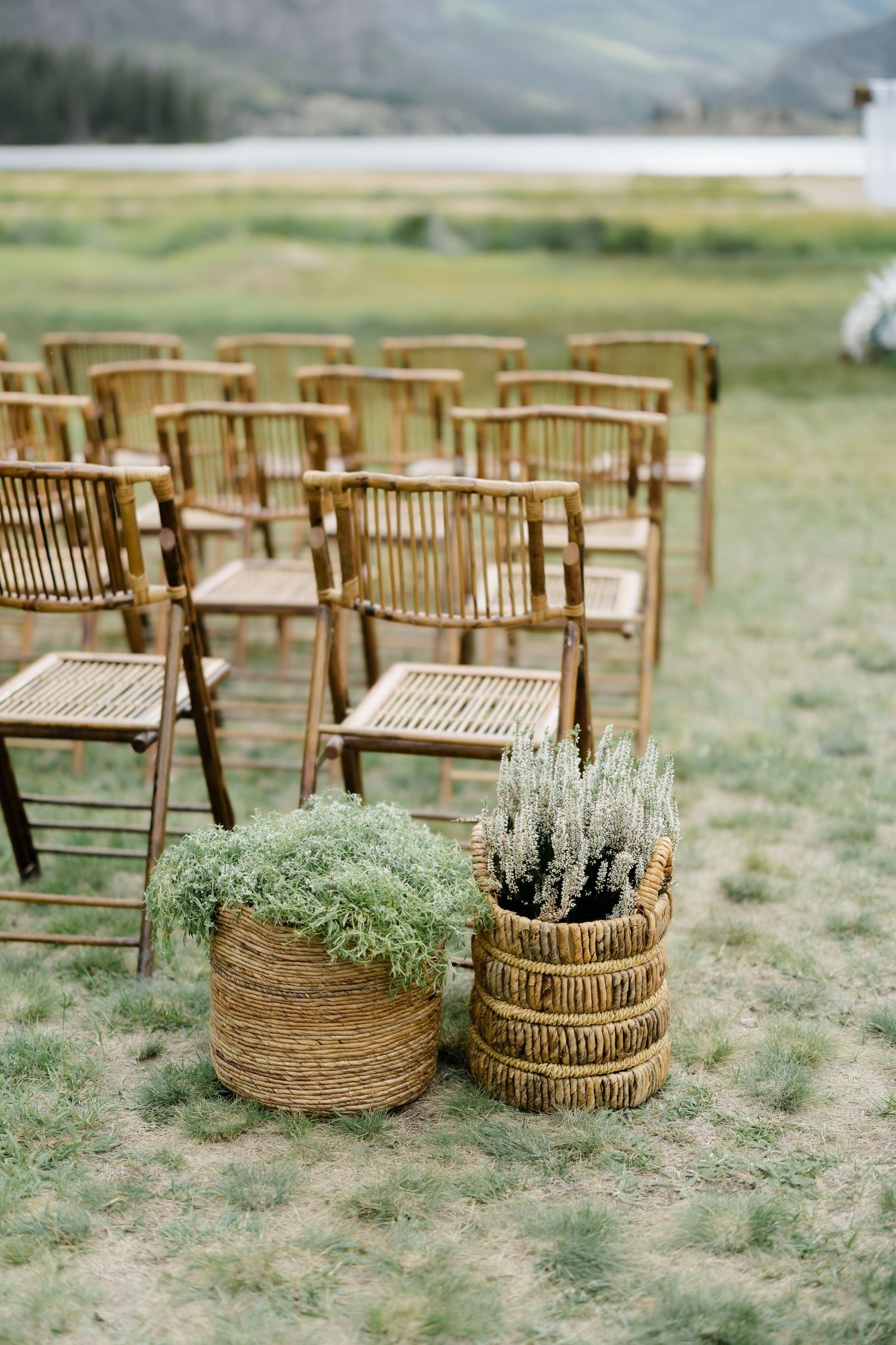 Rustic bamboo chairs arranged for an outdoor wedding ceremony with wicker baskets of greenery on grass.