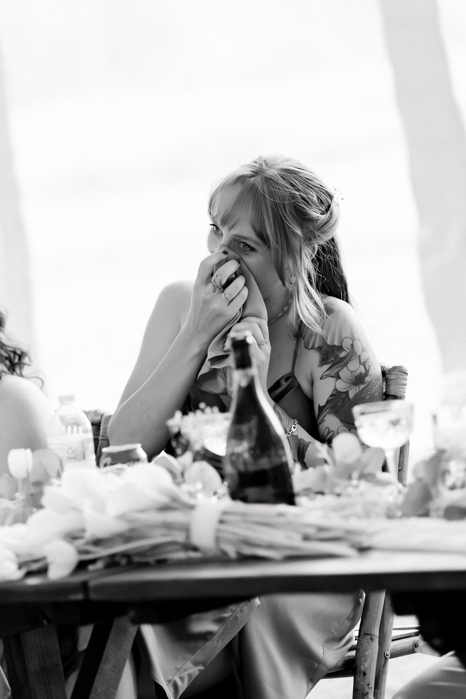 Black and white photo of a woman laughing at a wedding reception table with floral centerpieces.