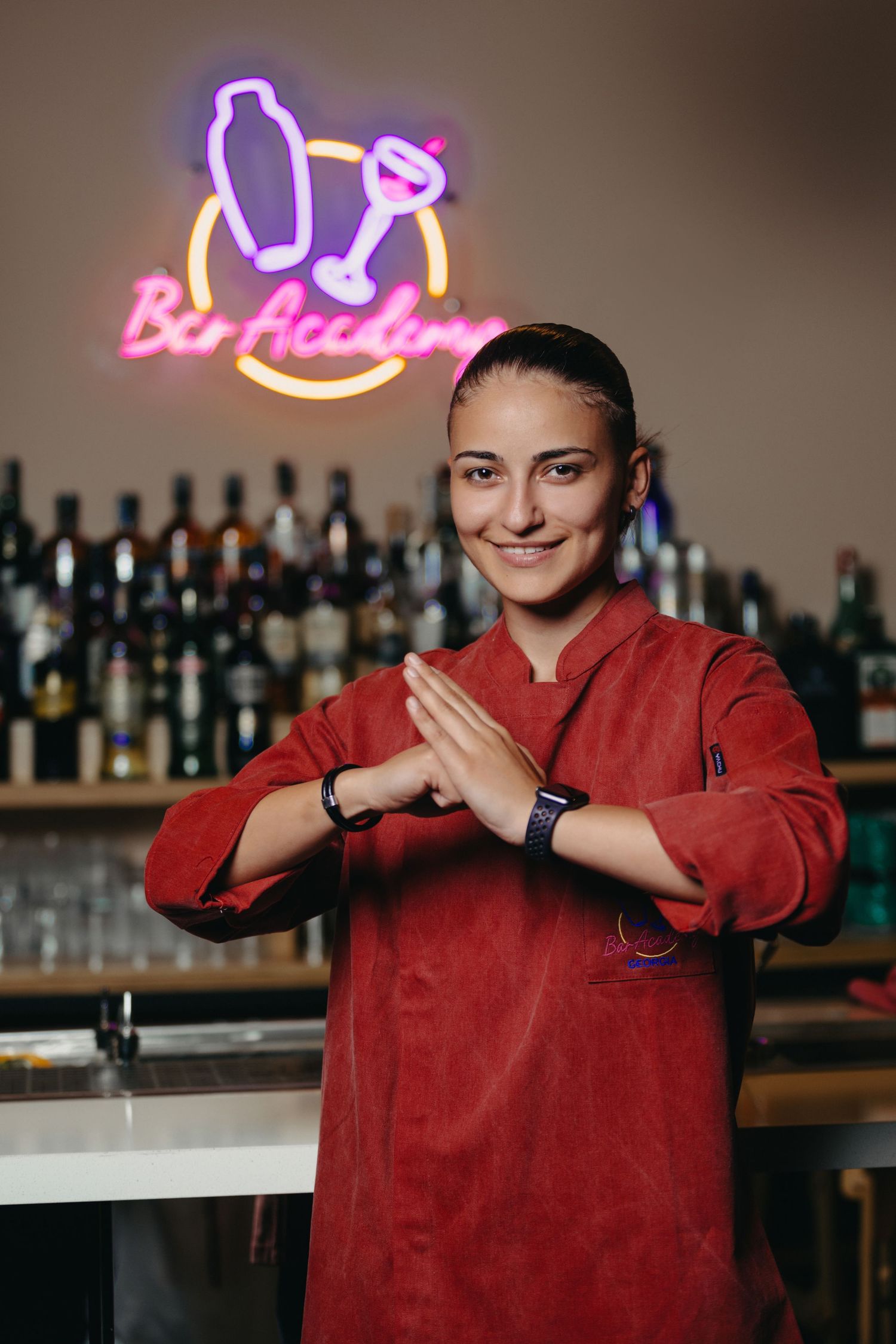 Bartender in red uniform demonstrates cocktail making techniques at a bar counter.