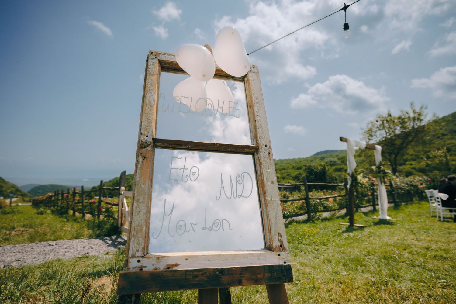 A rustic wooden sign frame decorated with white fabric against a blue sky.