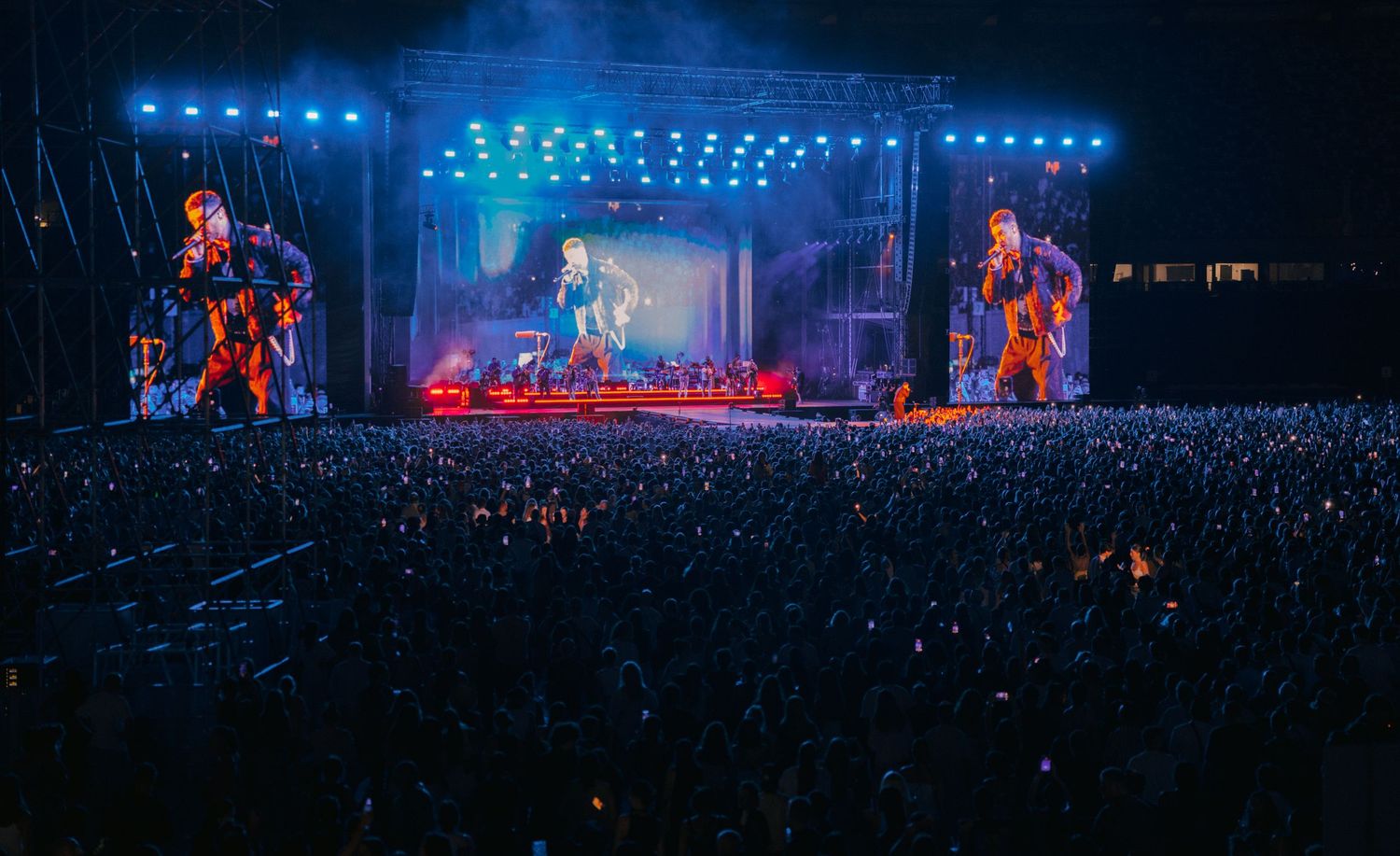 Concert stage lit with blue lights and crowd silhouetted against illuminated performance.