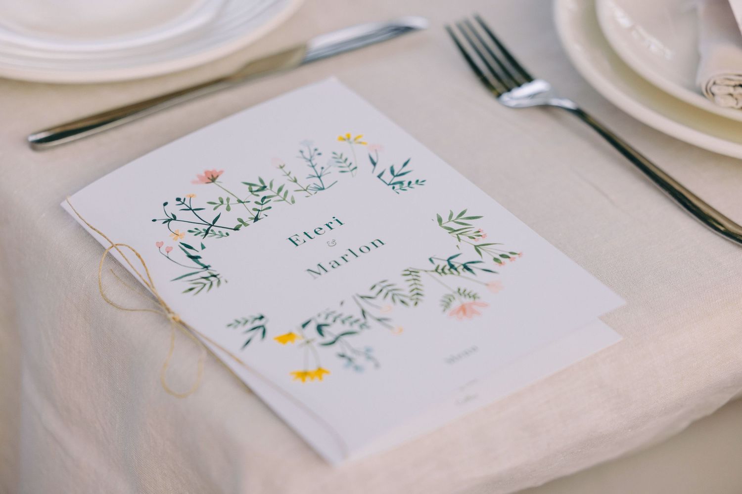 Elegant wedding place settings with floral decorated name cards and white plates on a table.