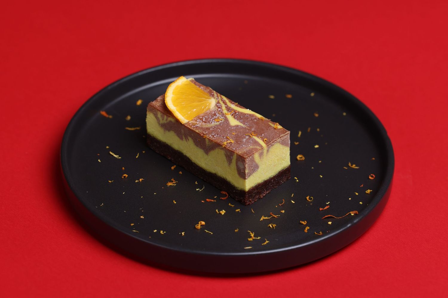 Progressive plating shots of citrus-garnished dessert on black plate against red background.