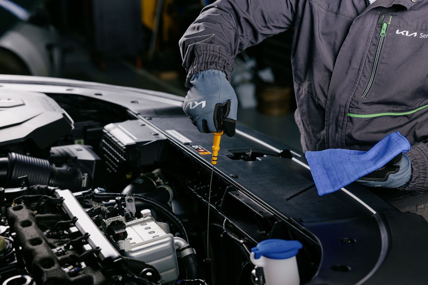 Kia mechanic in uniform checking engine oil level with dipstick during routine car maintenance service.