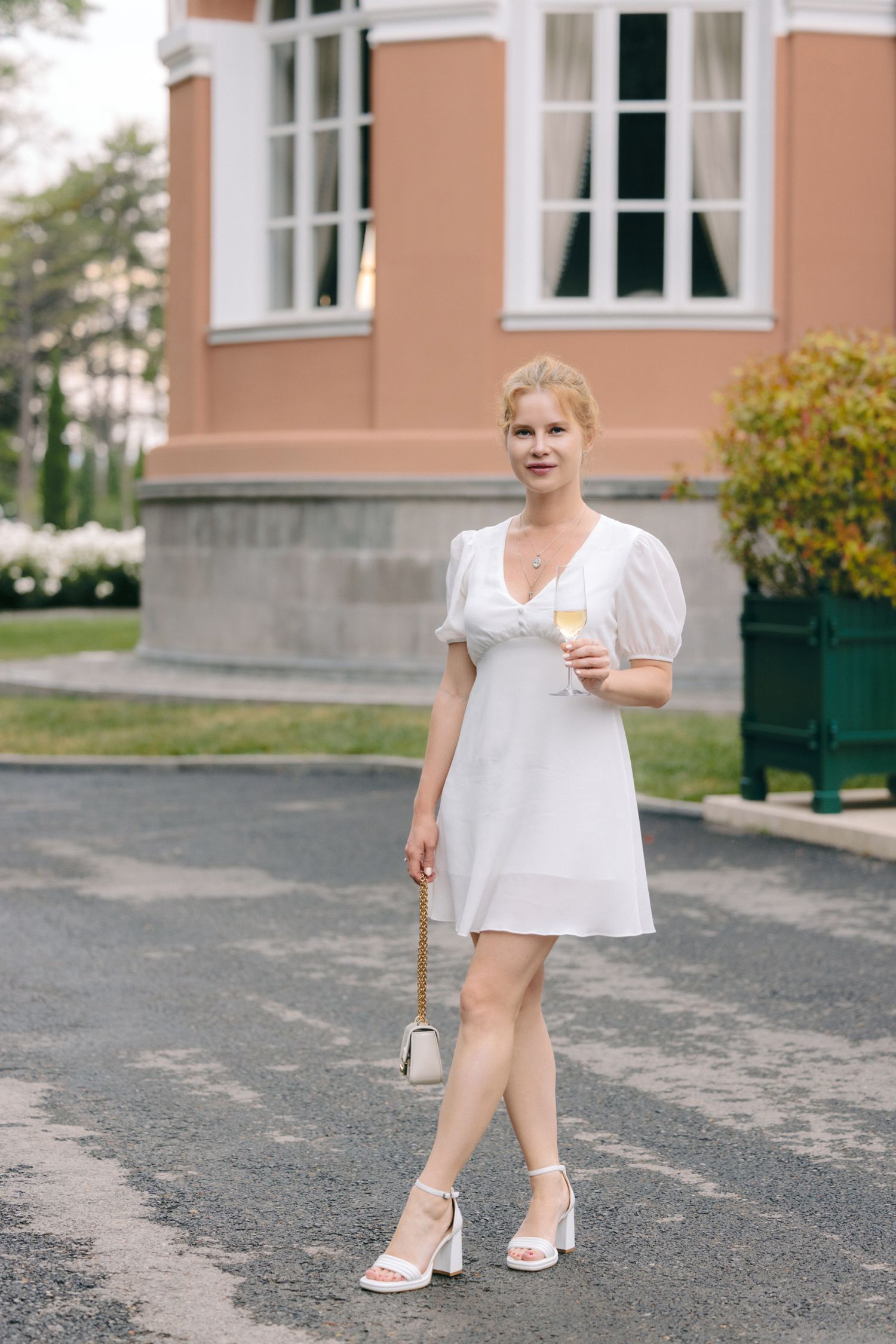 Elegant outdoor gathering with guests in white attire near a peach-colored building.