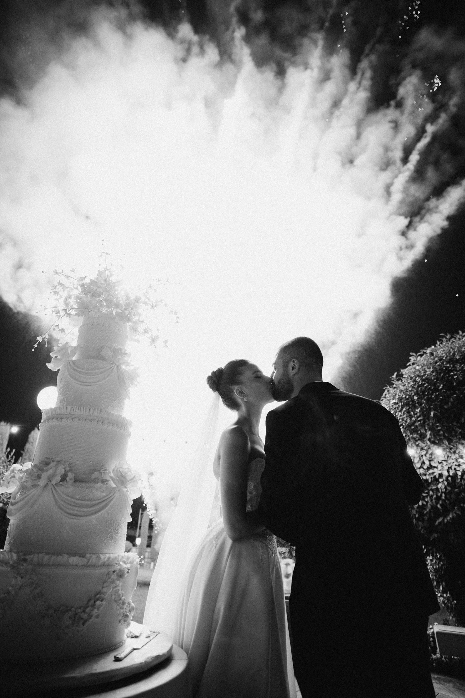 Wedding cake cutting moment captured in silhouette against bright sparkler effects.
