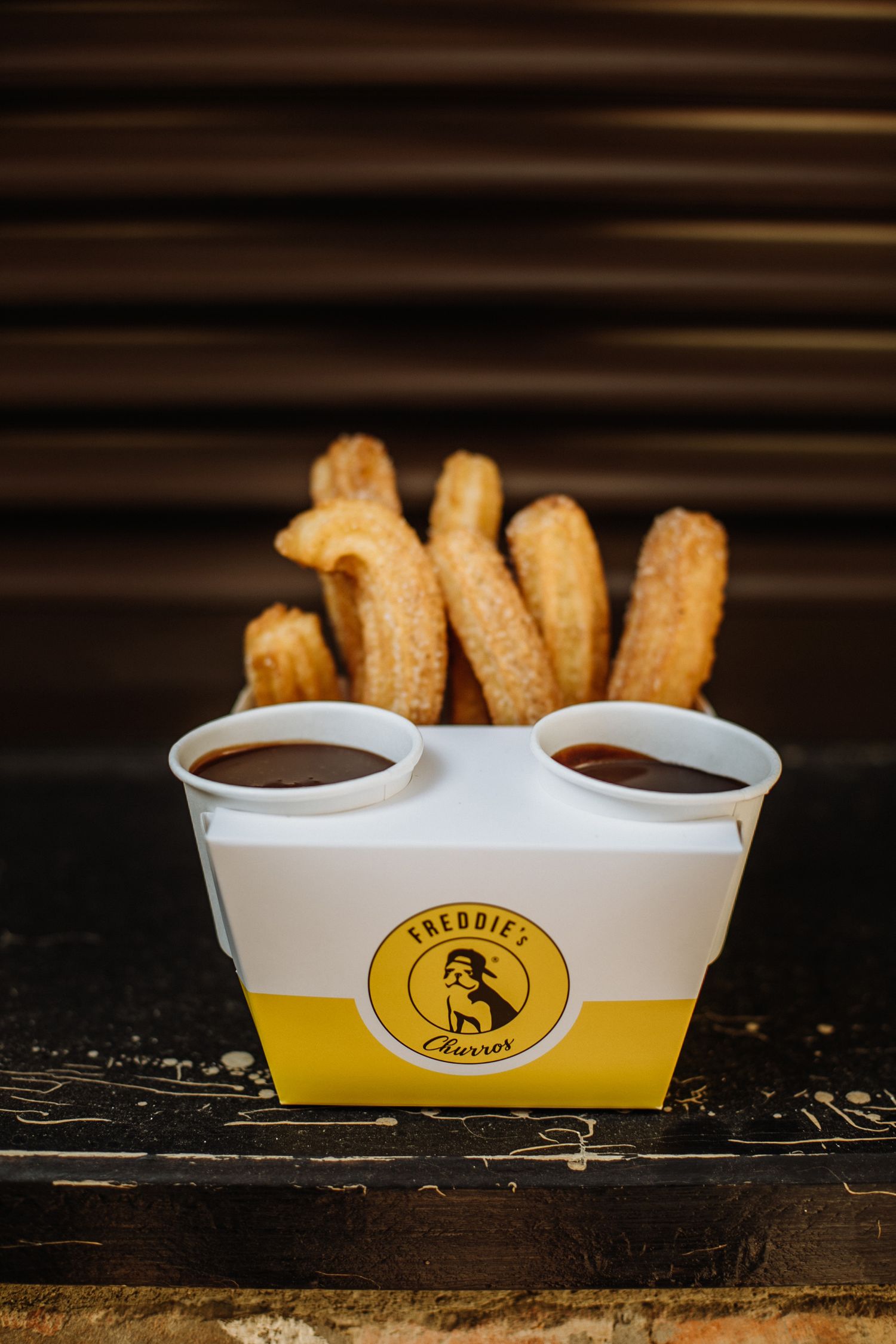 Churros served in yellow and white branded container with chocolate dipping sauce.