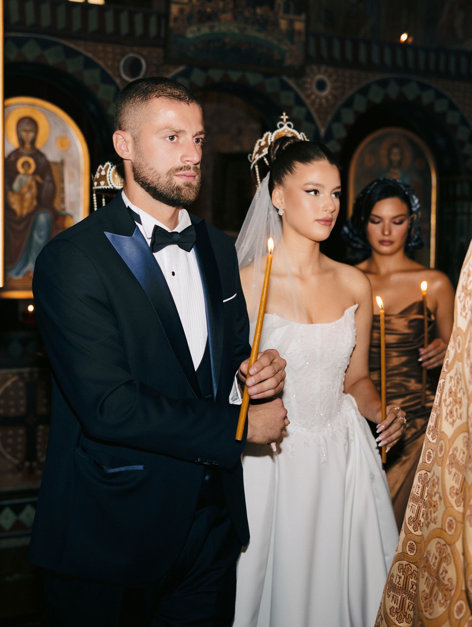 Elegant wedding ceremony in an Orthodox church with ornate religious icons in the background.