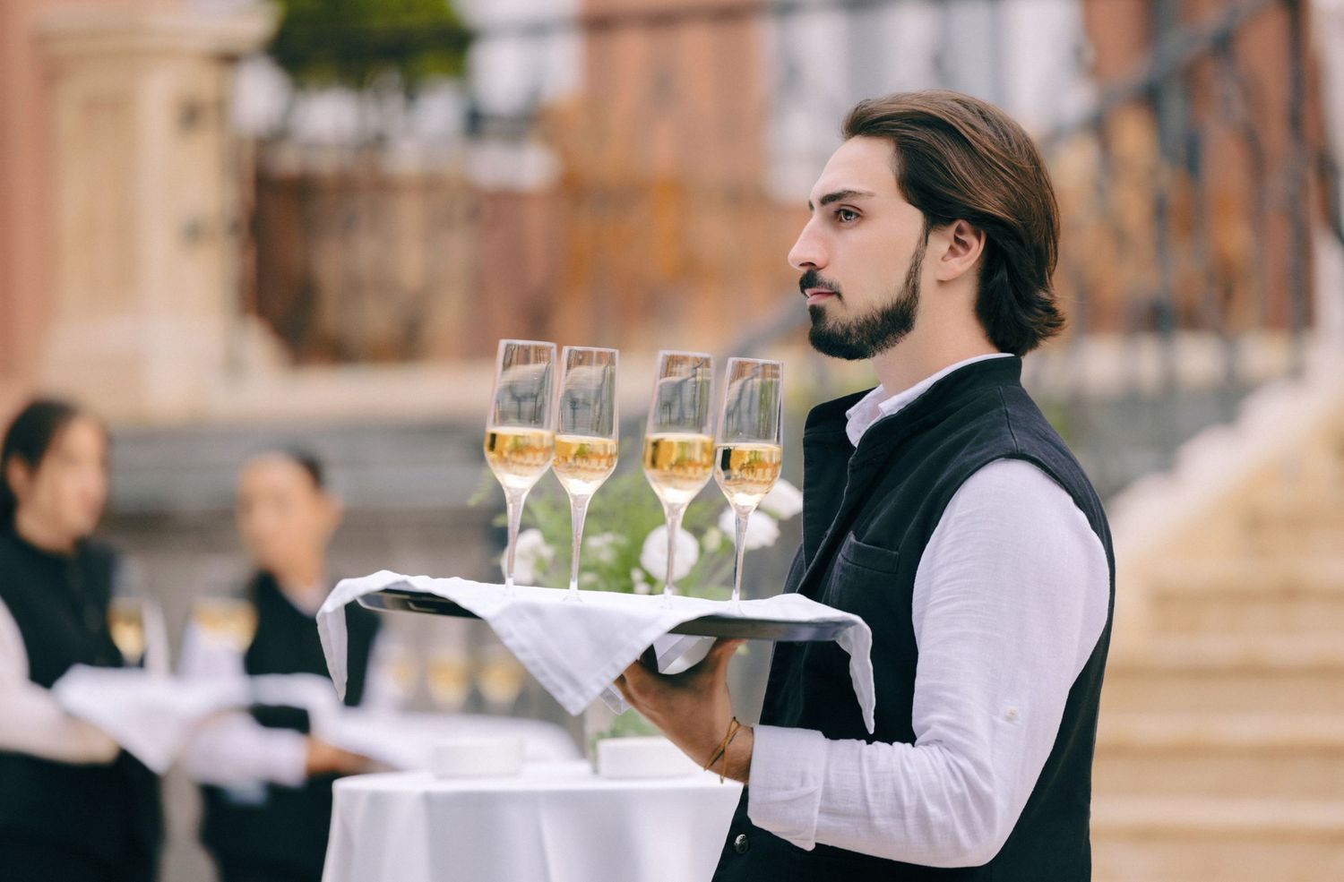 Waiters in black and white uniforms serving champagne at an outdoor event.