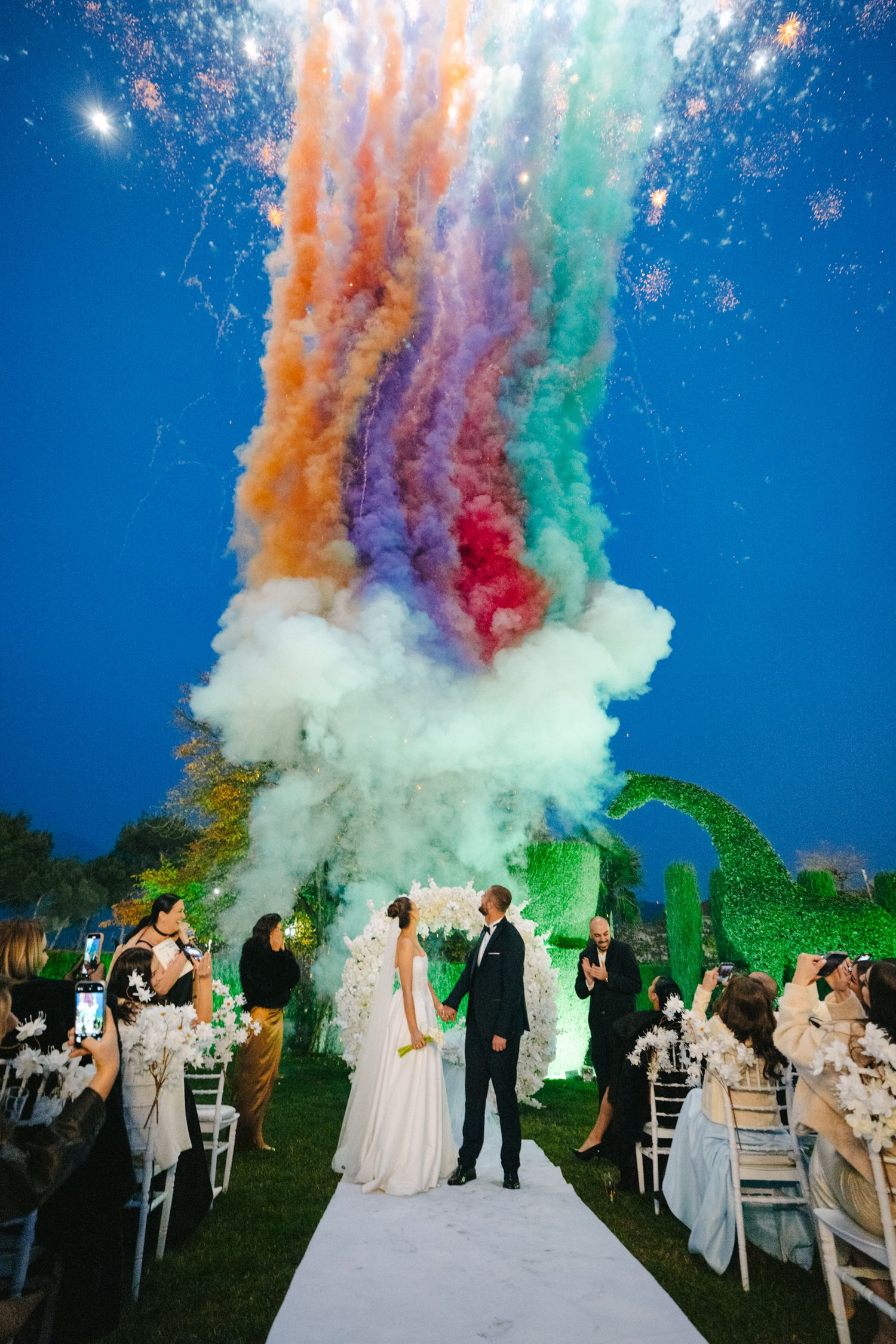 Dramatic colorful smoke effects create a magical atmosphere during an outdoor wedding ceremony.