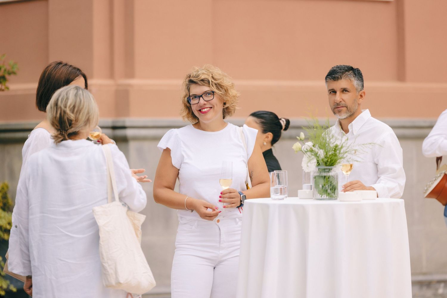 Guests mingling at an elegant outdoor party with white tables and decor.