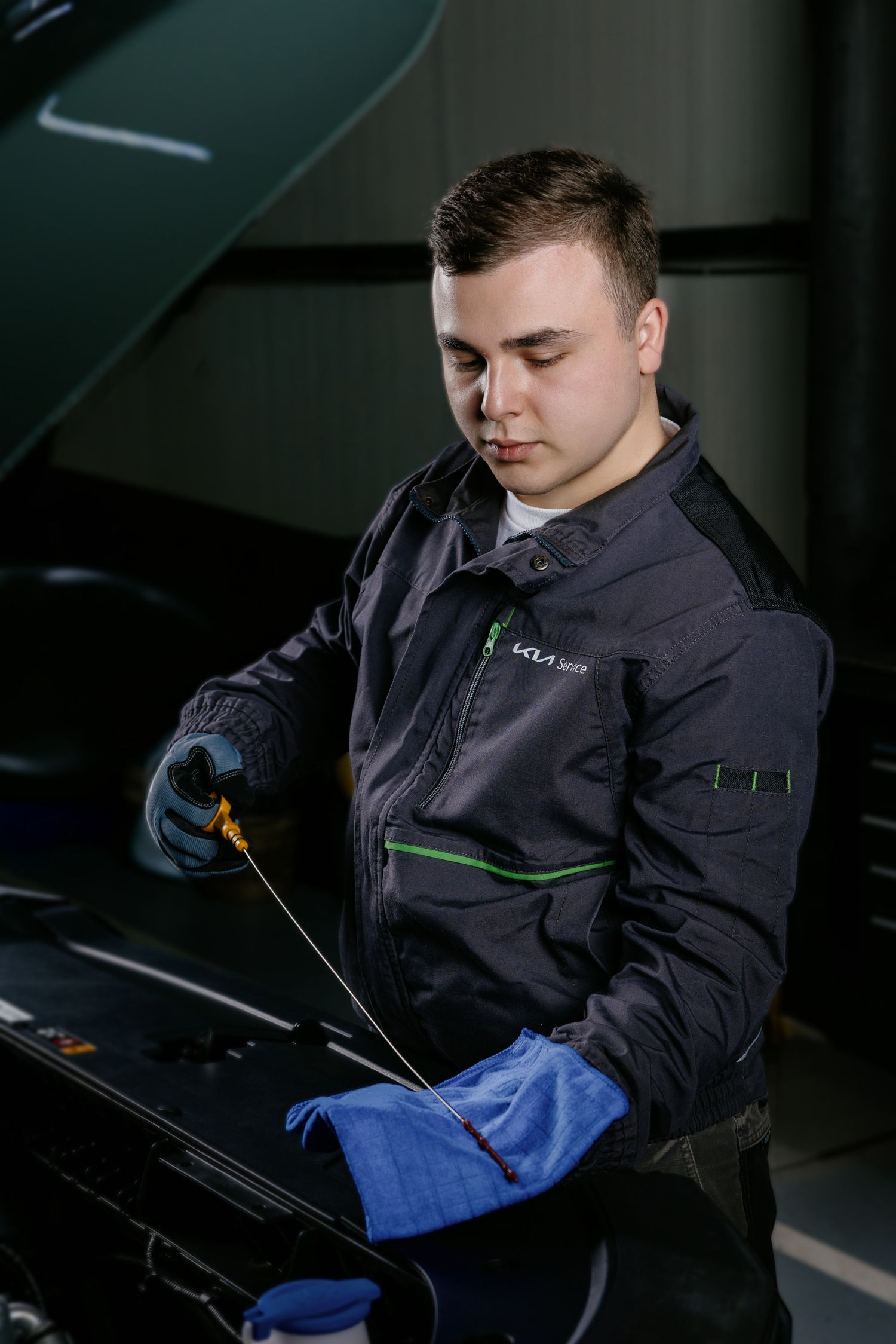 Young mechanic in uniform checks engine oil level with dipstick at auto service garage.