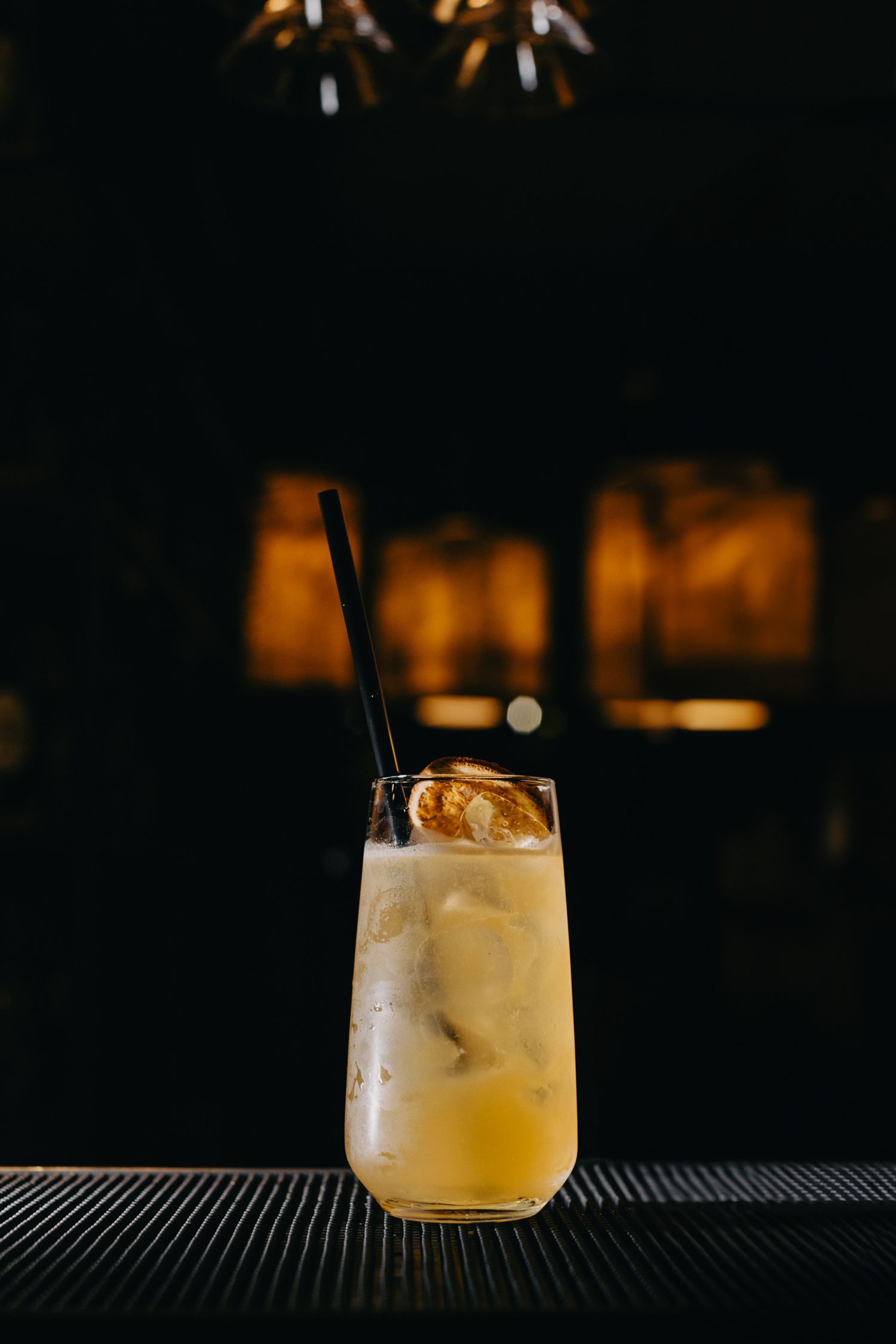 Golden cocktails with ice cubes served on a black bar surface in dim lighting.