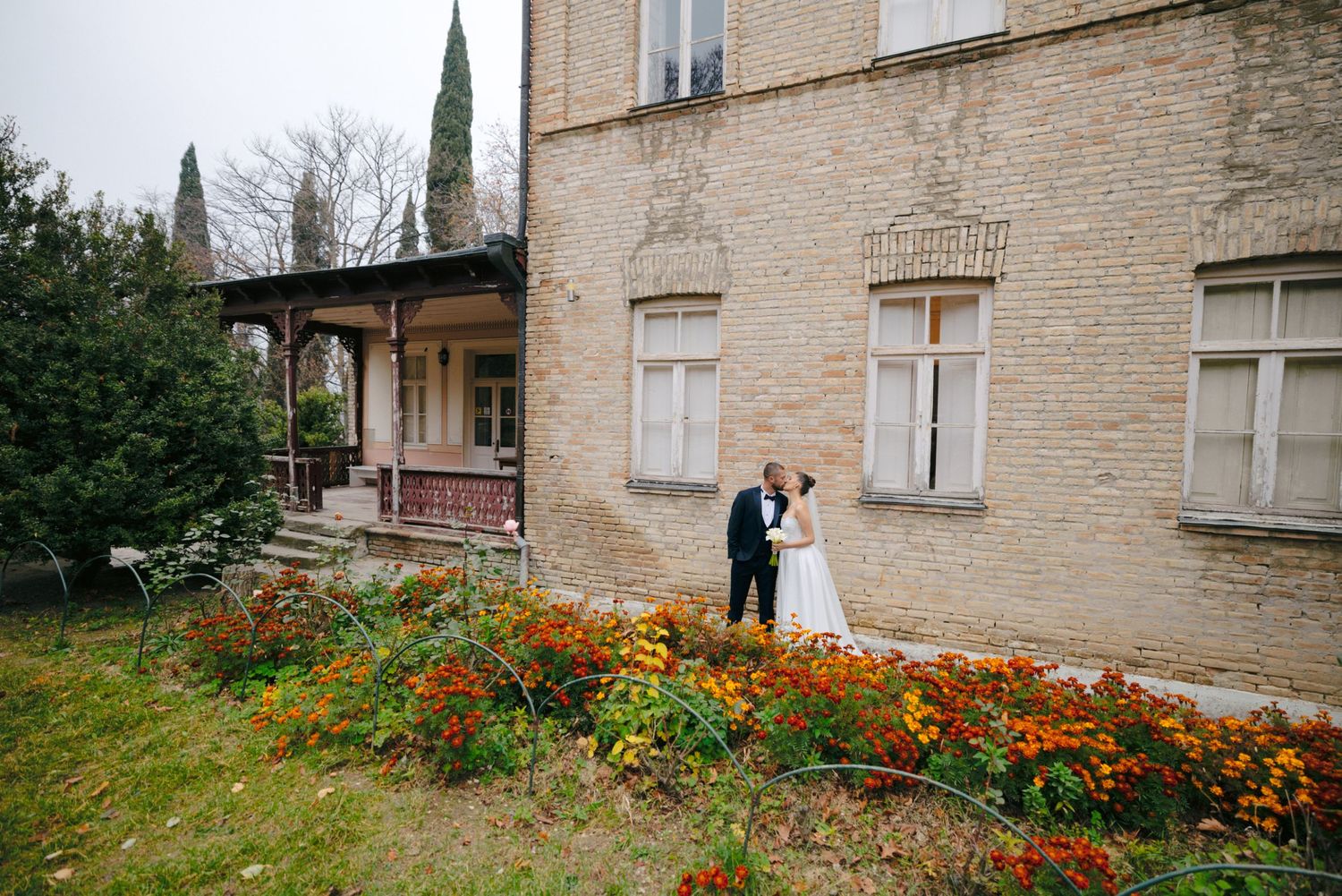 Elegant wedding scene with couple by vintage building and vibrant marigold garden.