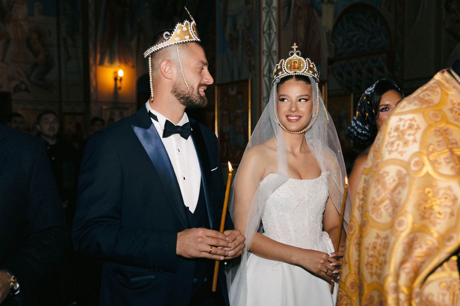 Traditional Orthodox wedding ceremony with bride in white dress and veil holding candles.