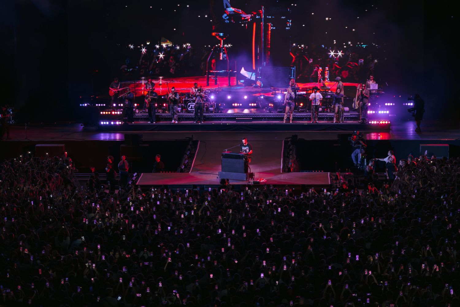 Stadium concert at night with colorful stage lighting and sea of audience members.