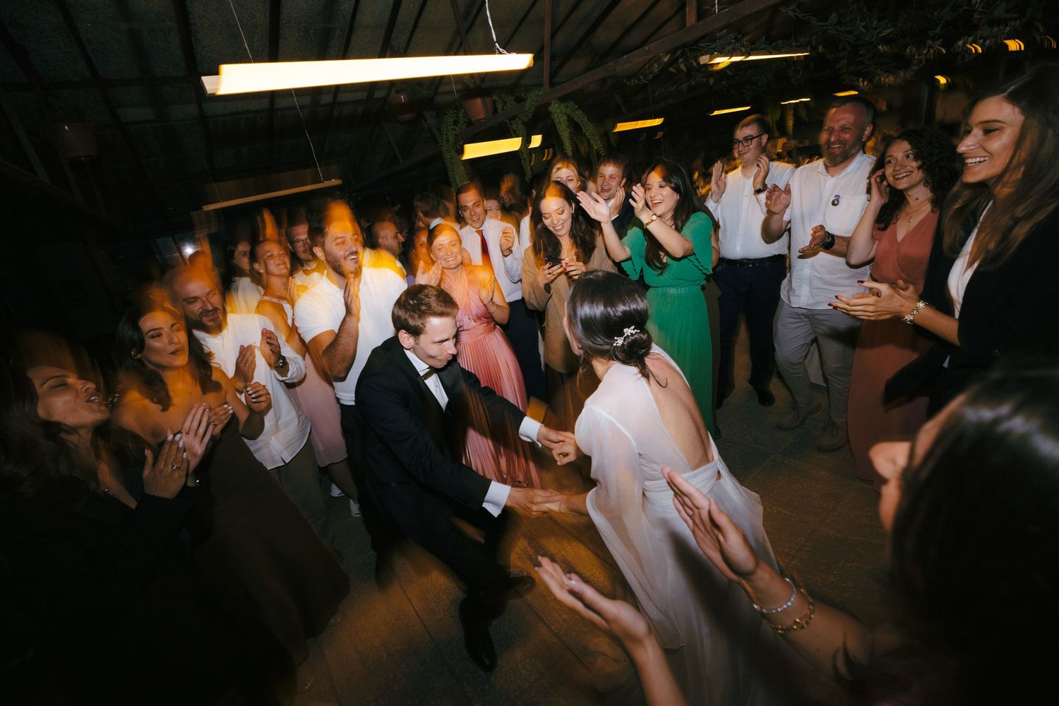 Wedding reception dance party with guests celebrating in a dimly lit venue.