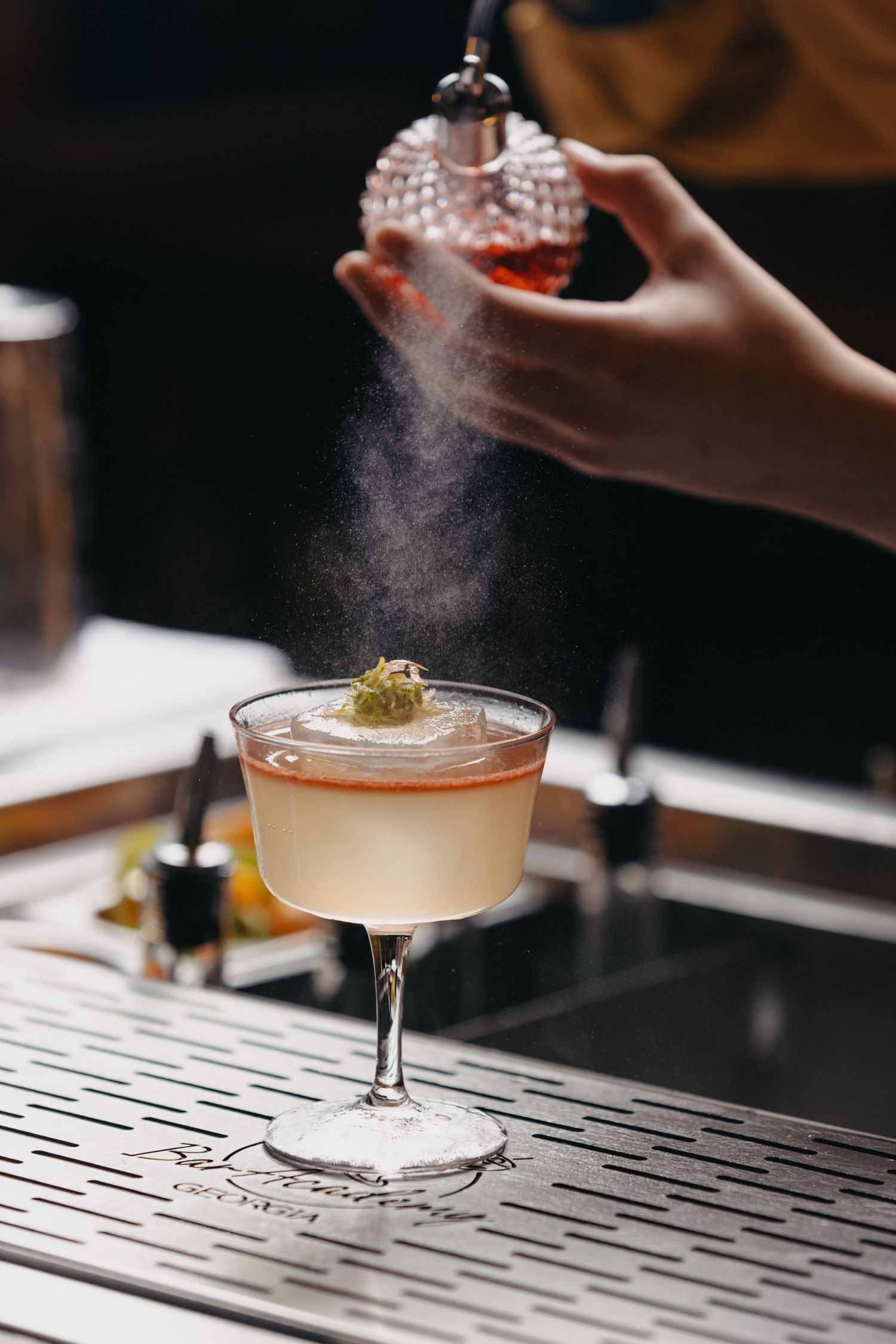 Elegant cocktail being garnished with powder on dark bar counter.