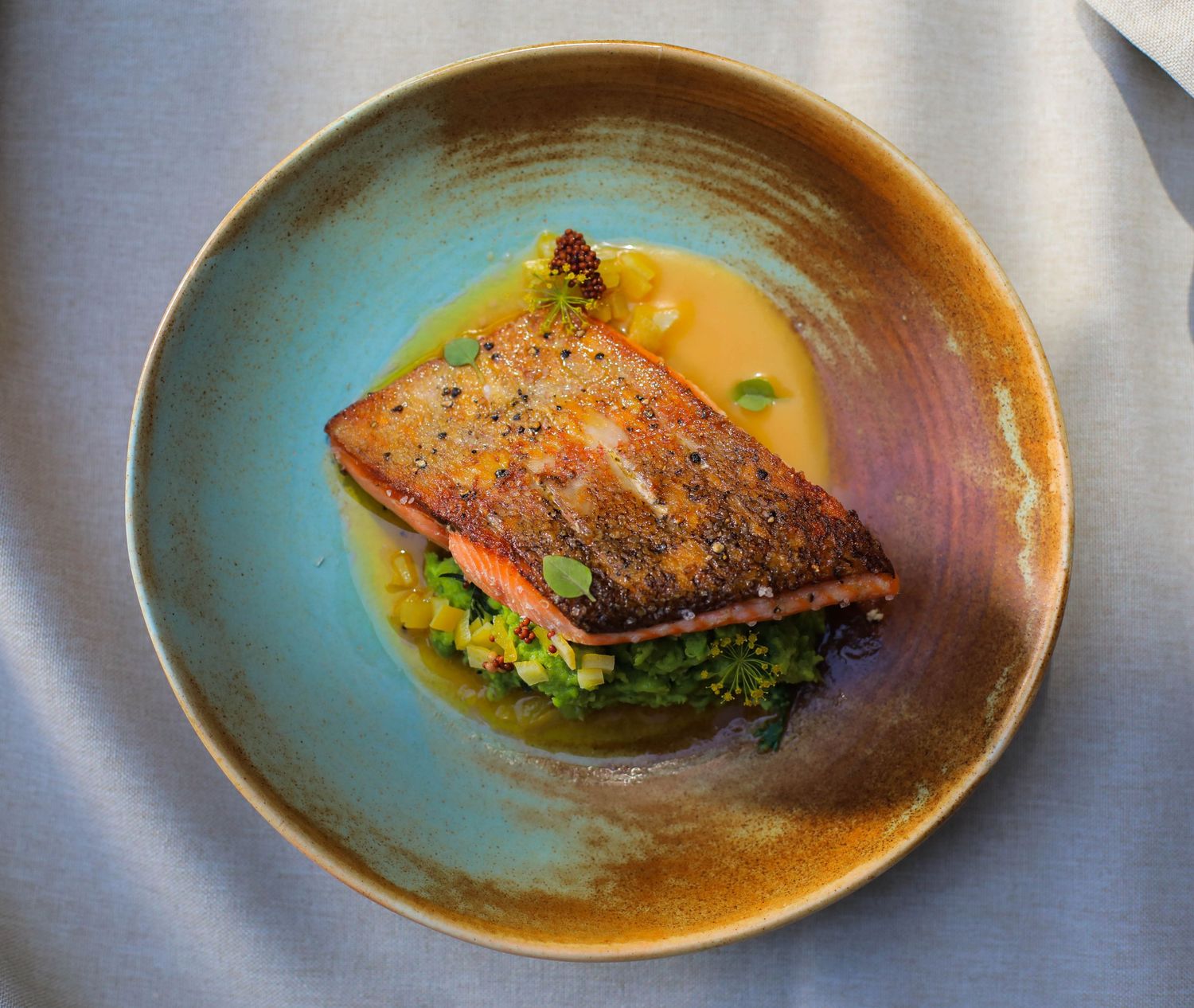 Gourmet fish dish served on turquoise ceramic plate with sauce and garnish.