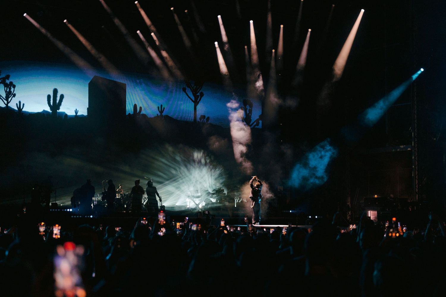 Concert stage lit up at dusk with dramatic lighting and desert cacti silhouettes in the background.