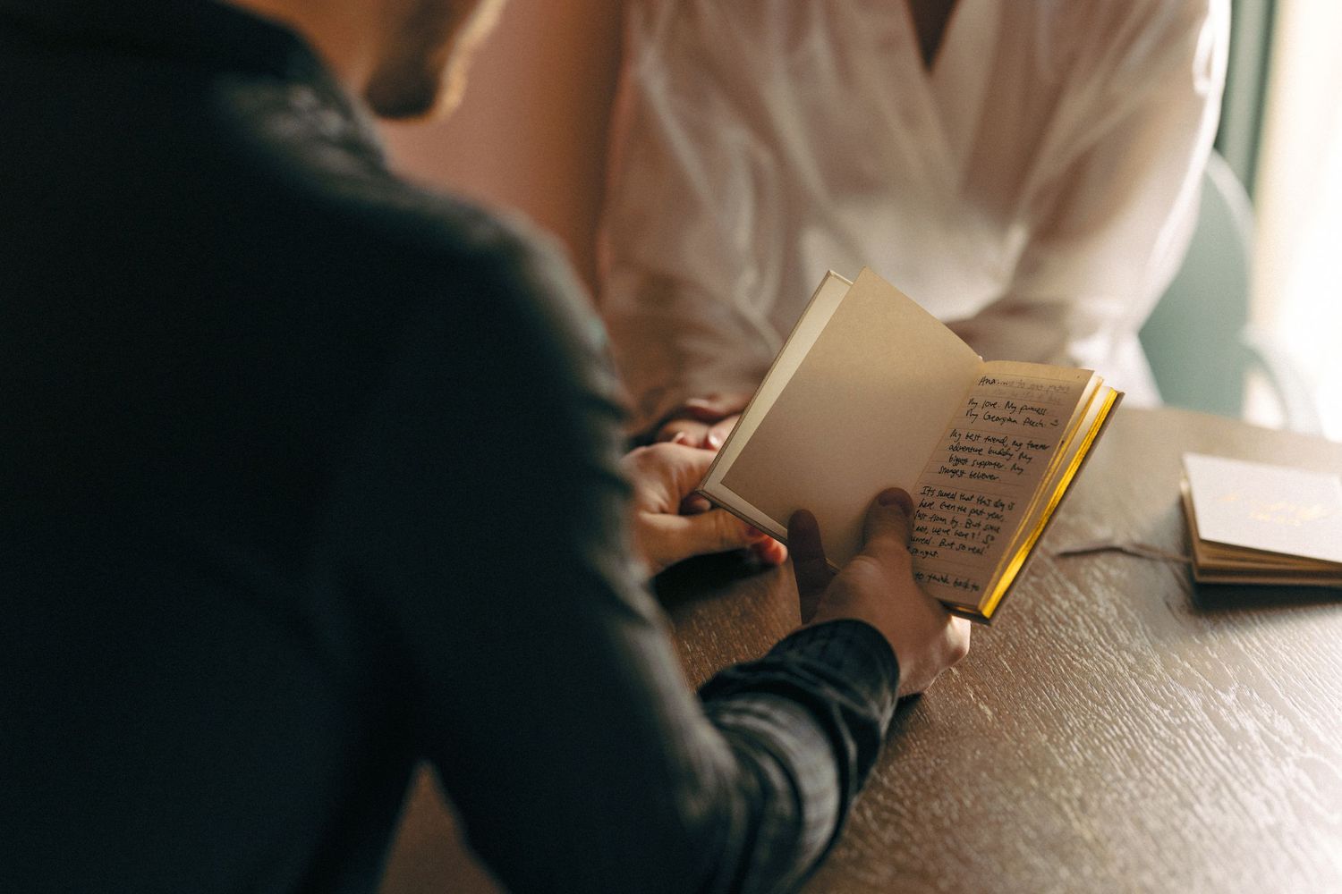 Person in white dress reads from book or document in natural lighting.