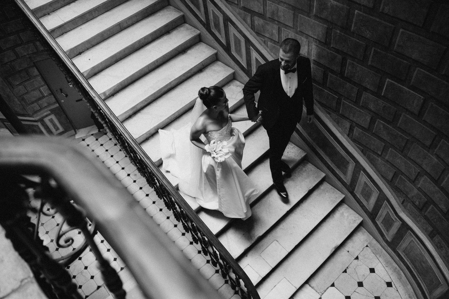 Dramatic black and white photo of wedding couple descending stone staircase.
