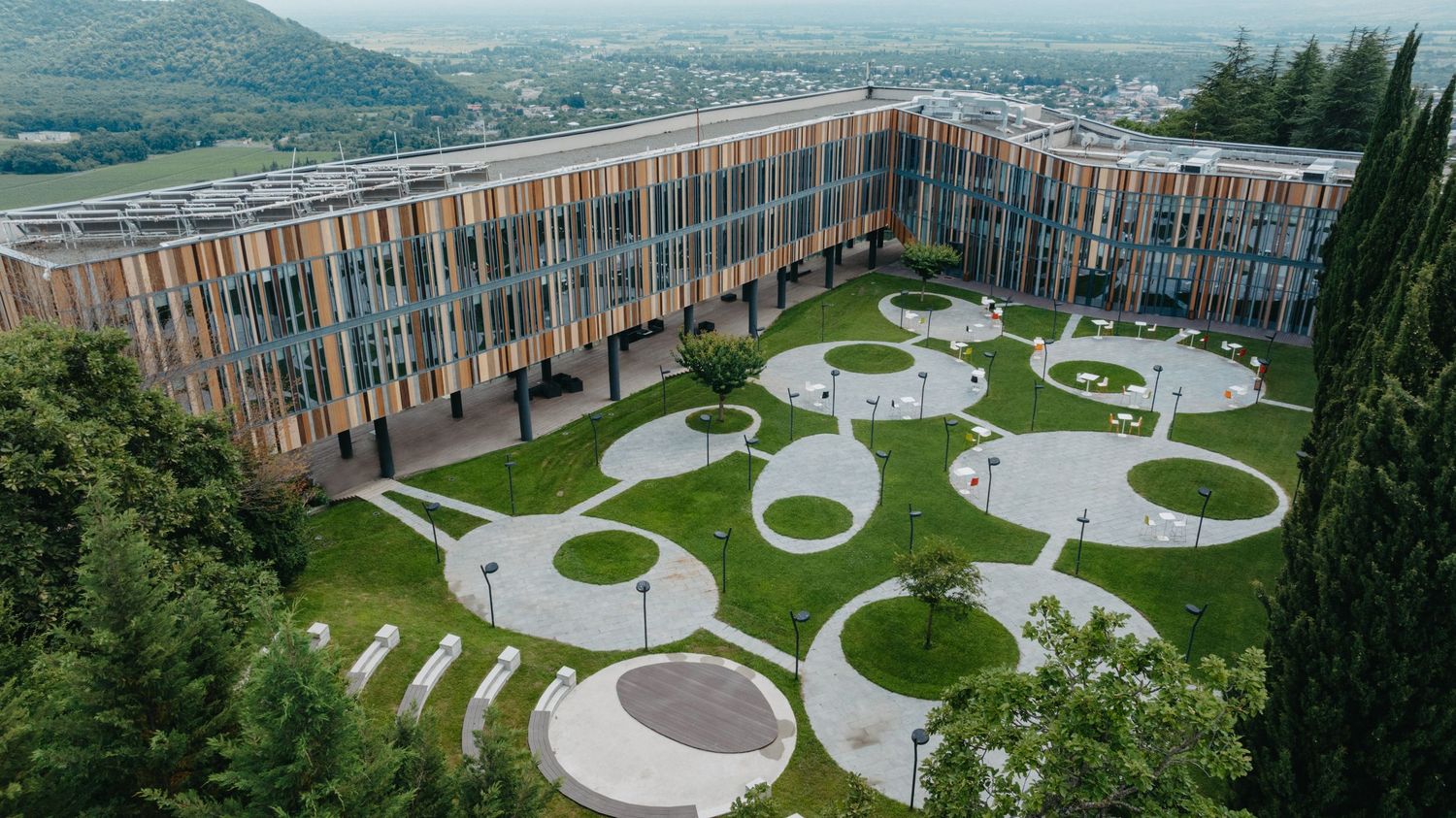 Aerial panorama of a modern building complex with circular garden features and mountain views.