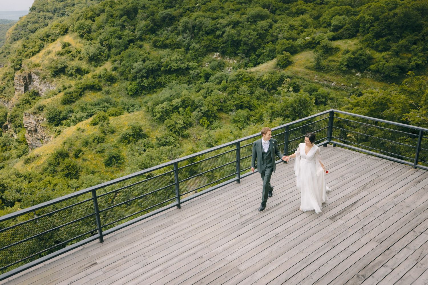 Couple walking along a wooden observation deck with sweeping mountain vistas in the background.