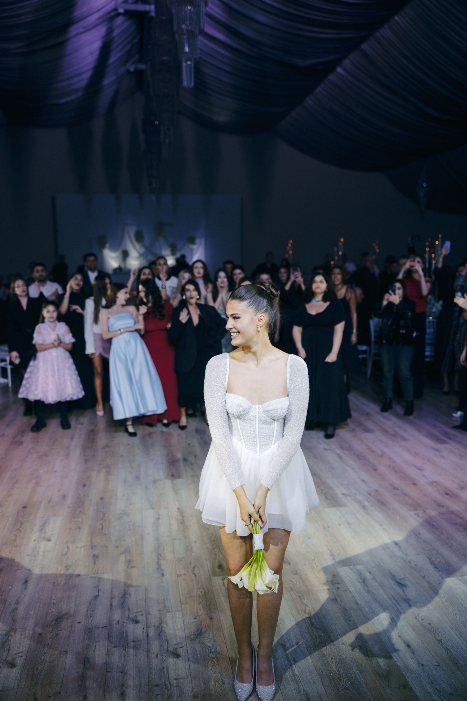 Wedding reception dance floor scene with guests in formal attire under purple lighting.
