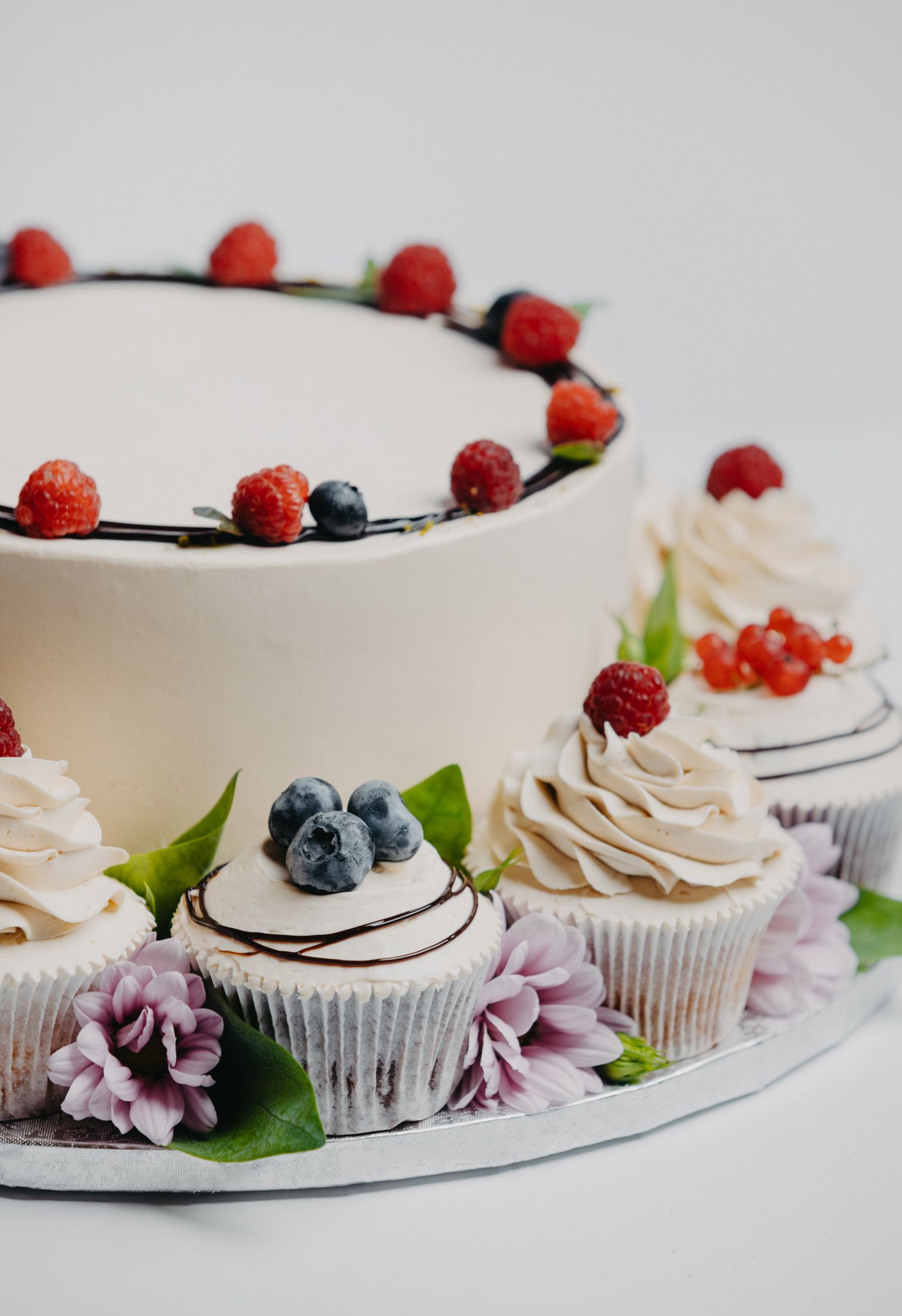 Beautifully decorated cupcakes with berries and floral garnishes arranged in a line.