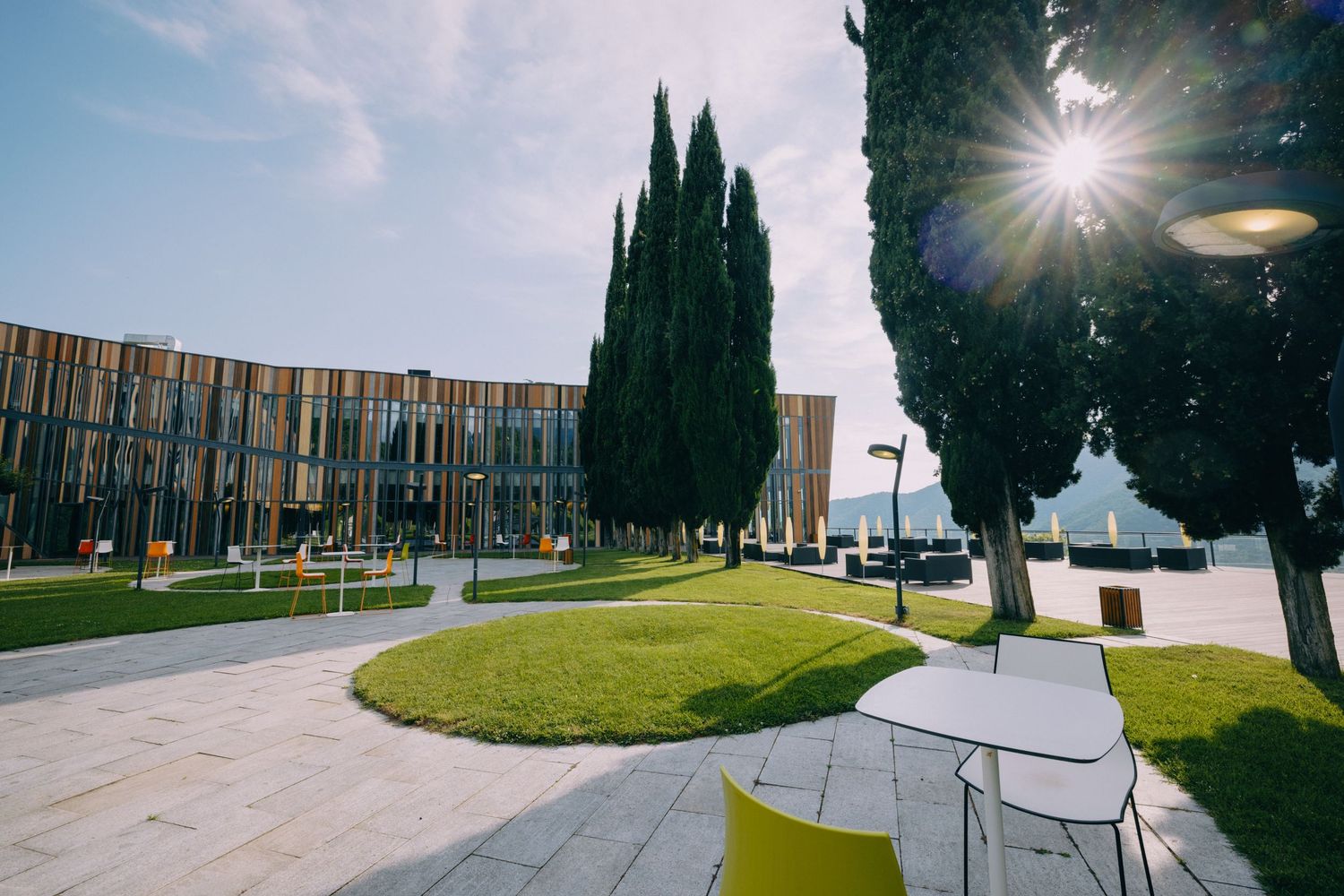 Modern architectural building with glass facade and landscaped grounds featuring curved pathways and green spaces.